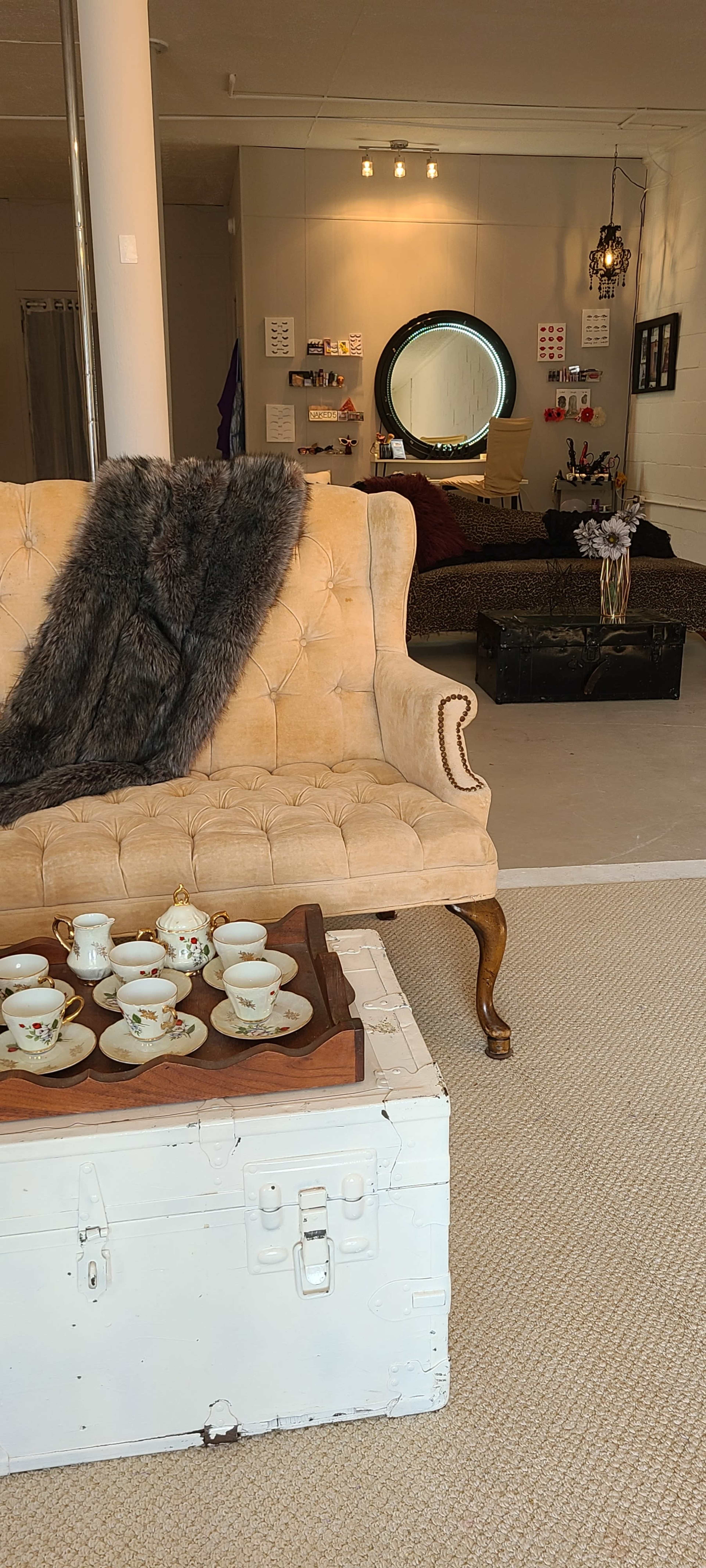 A vintage-style sofa and decorative tea set are positioned in a softly lit room, with a round mirror and various decorative items in the background.