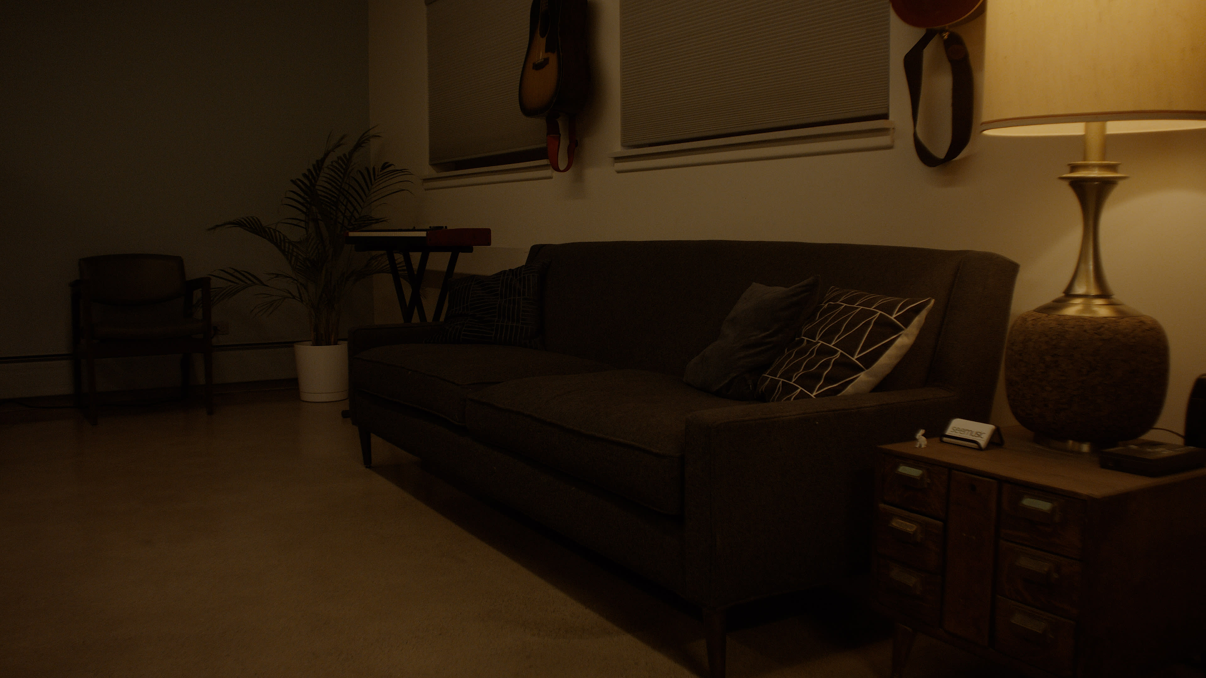 The image shows a dimly lit living room with a dark sofa, a small table, a lamp, and a keyboard in the corner.