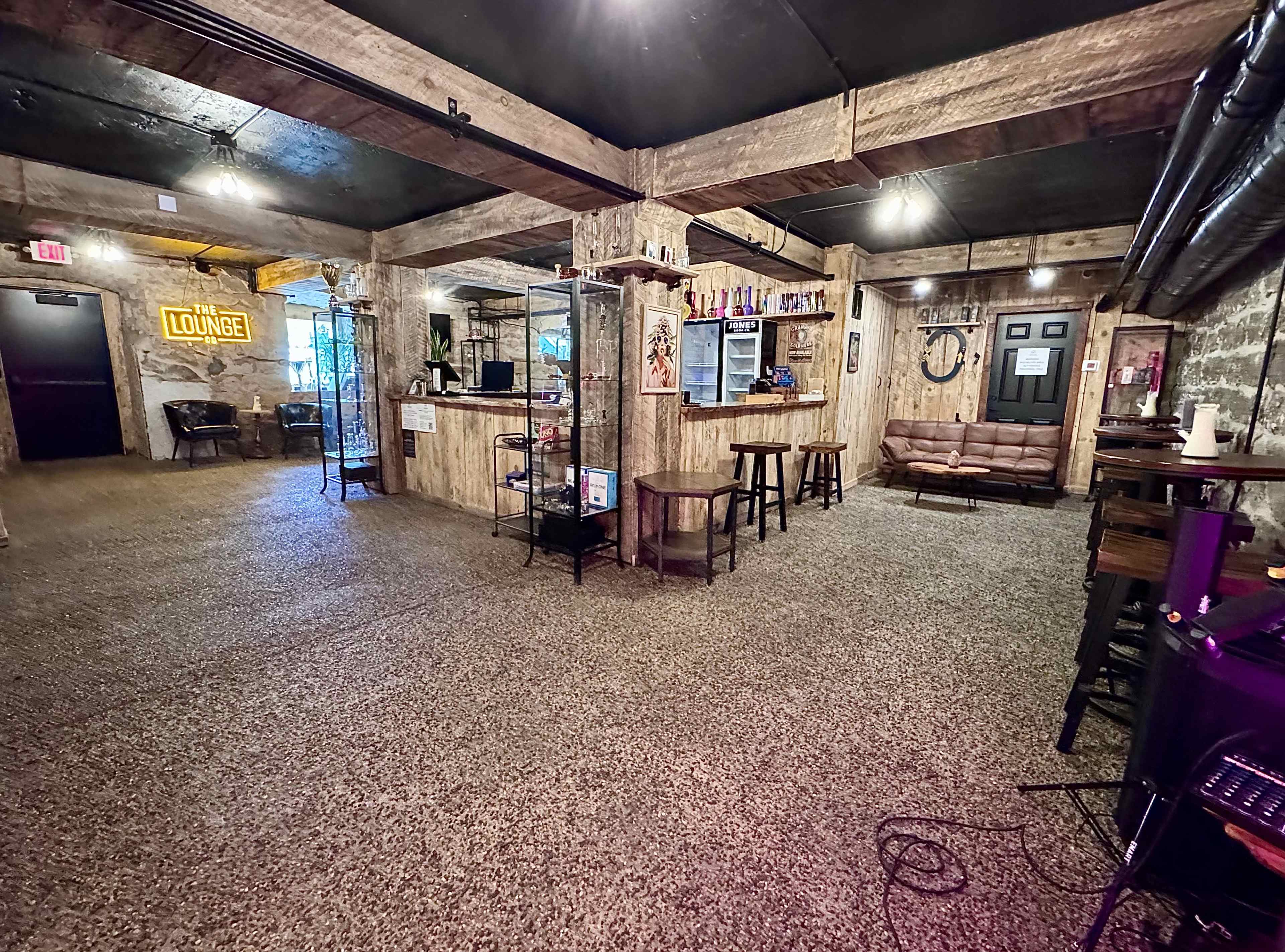 The image shows a spacious, rustic lounge area featuring wooden walls, a couch, and various furnishings arranged in an open layout.