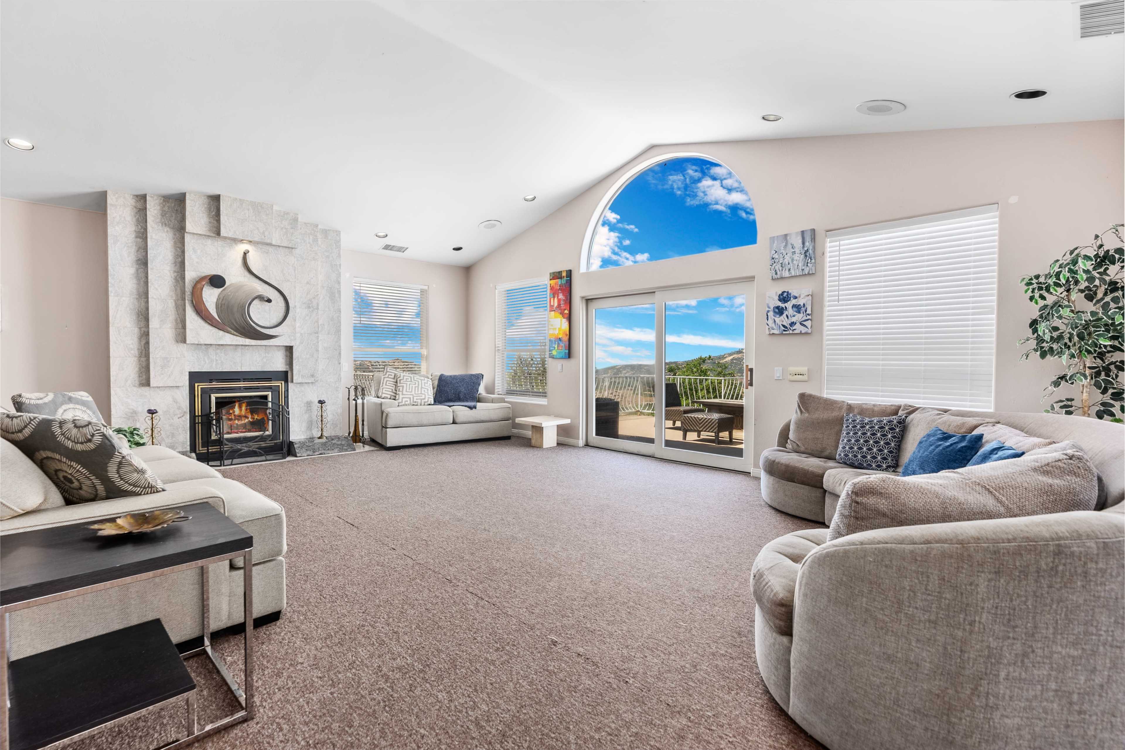 The living room features two light-colored sofas, a stone fireplace, and large windows with a view of the outdoors.
