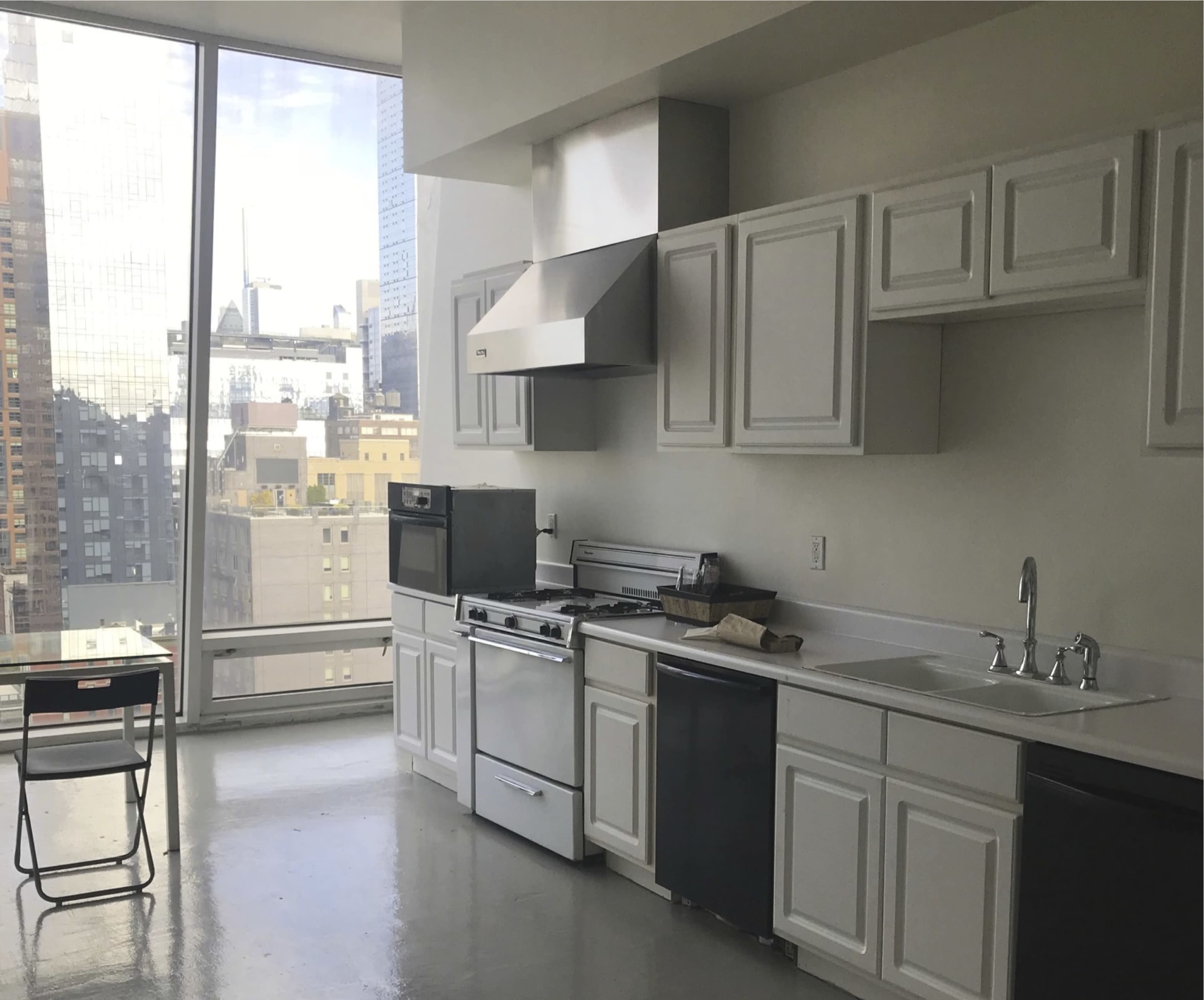 A modern kitchen features white cabinets, stainless steel appliances, and a large window with a view of the city skyline.