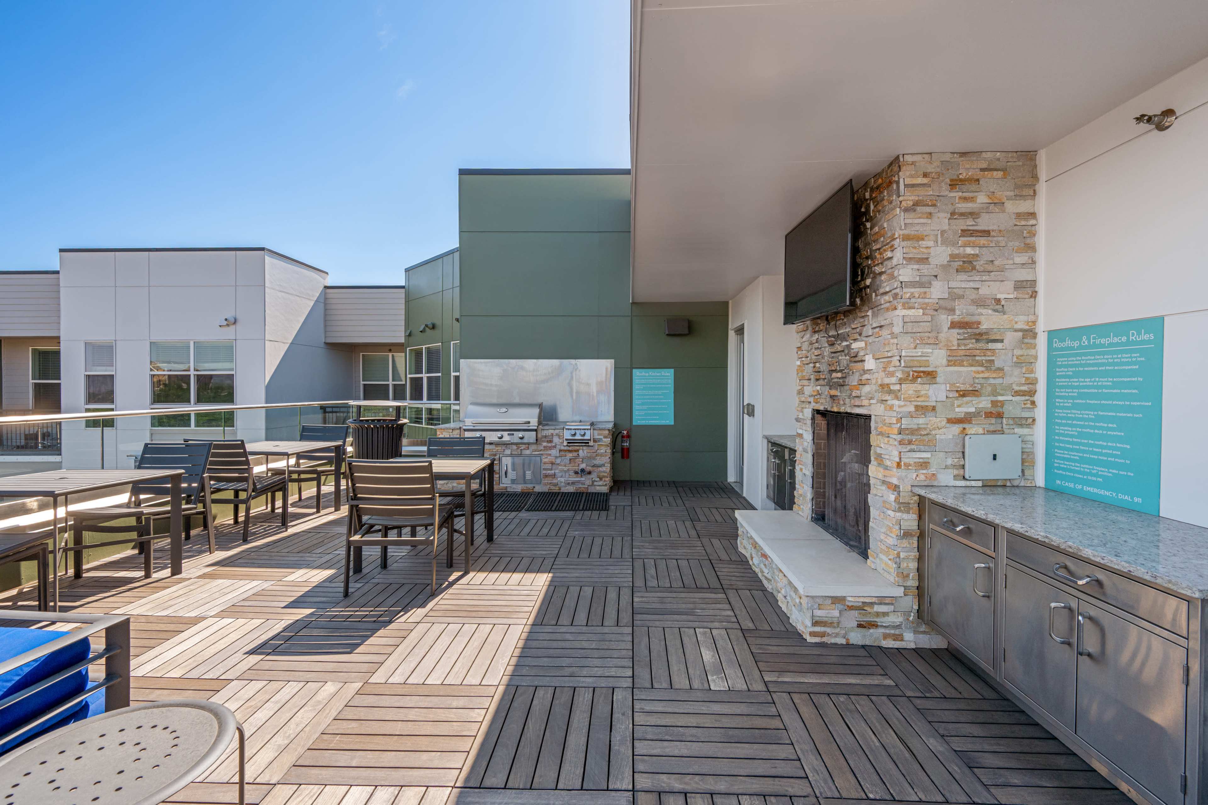 The image shows a modern outdoor patio area featuring a grill, seating, and a fireplace, surrounded by walls of green and beige.
