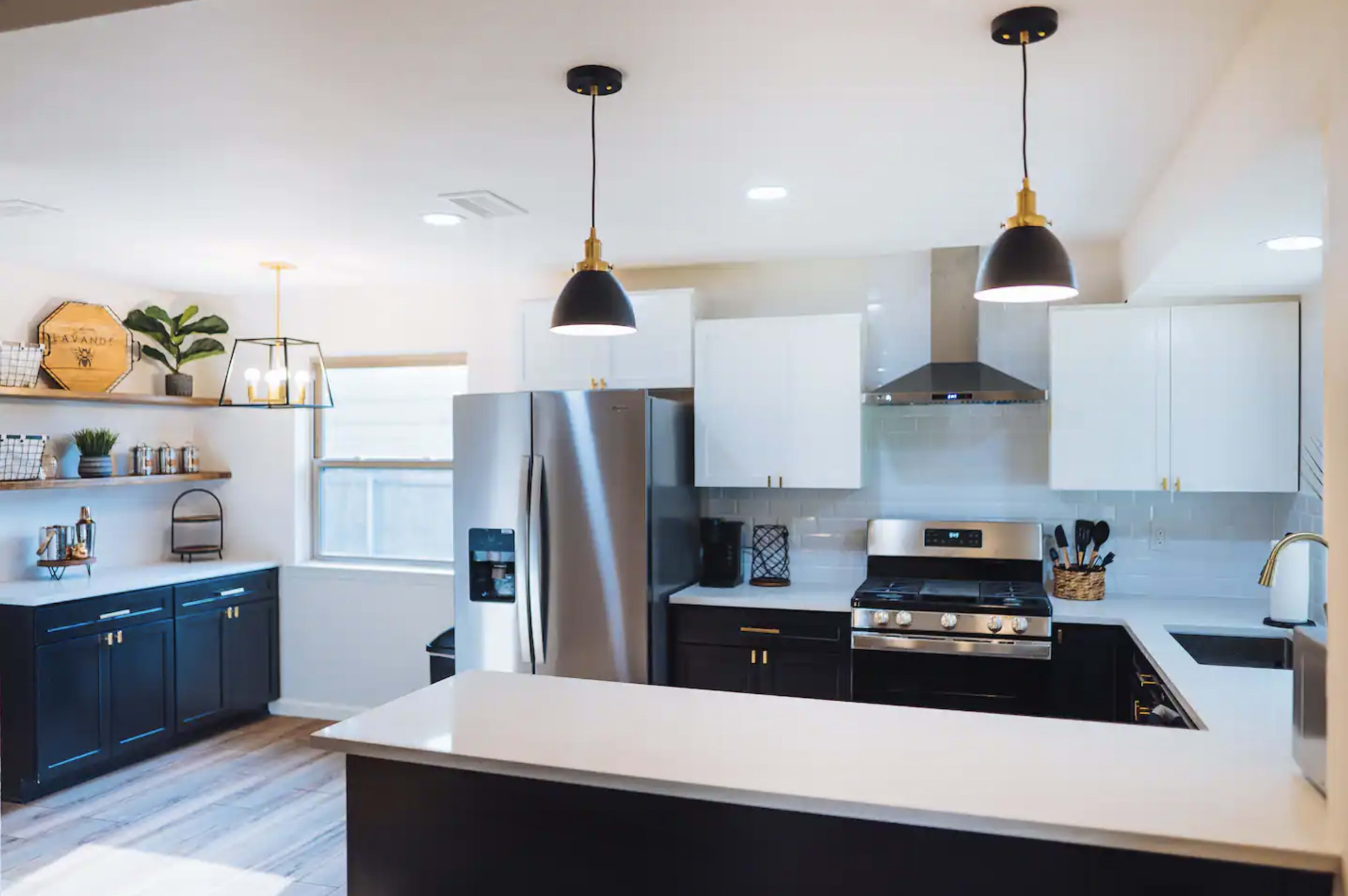A modern kitchen with stainless steel appliances, white upper cabinets, black lower cabinets, and pendant lighting.