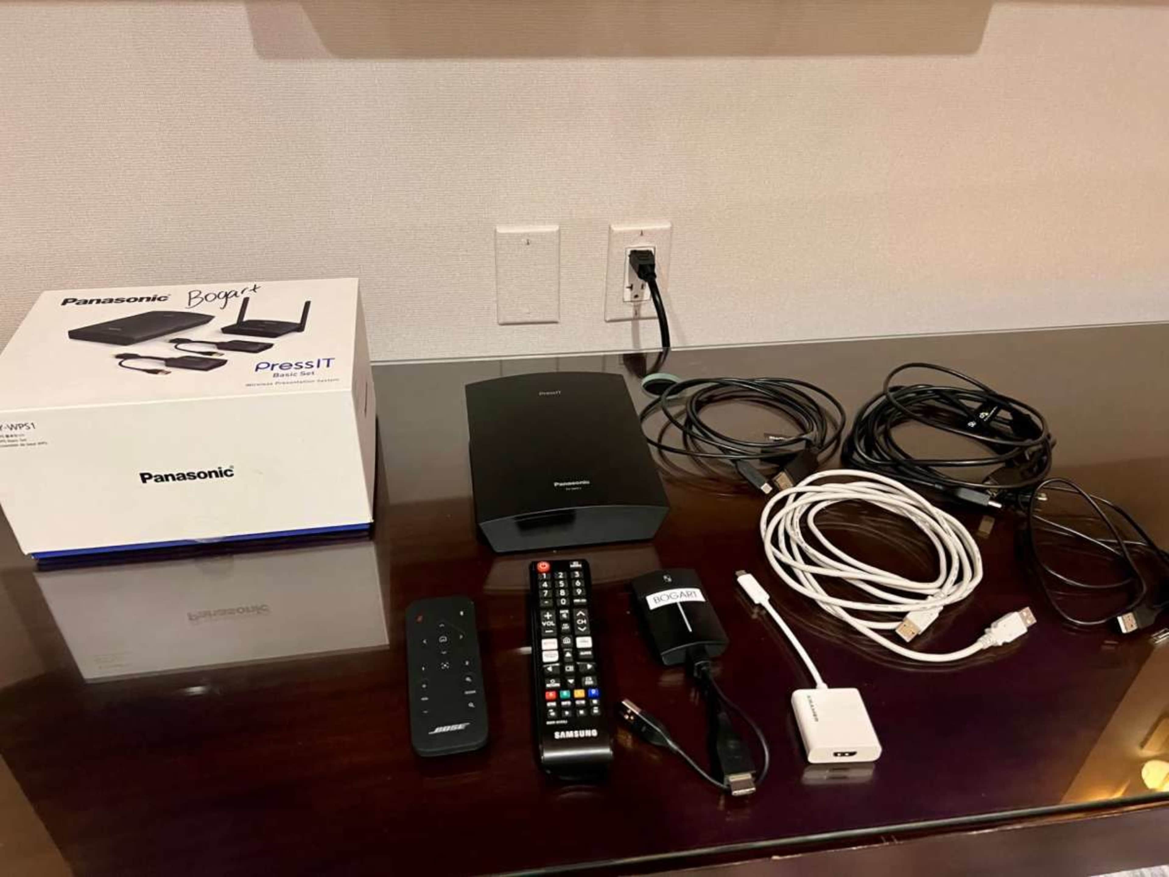 The image shows a Panasonic PressIT presentation device along with various cables, a remote control, and other accessories arranged on a wooden surface.