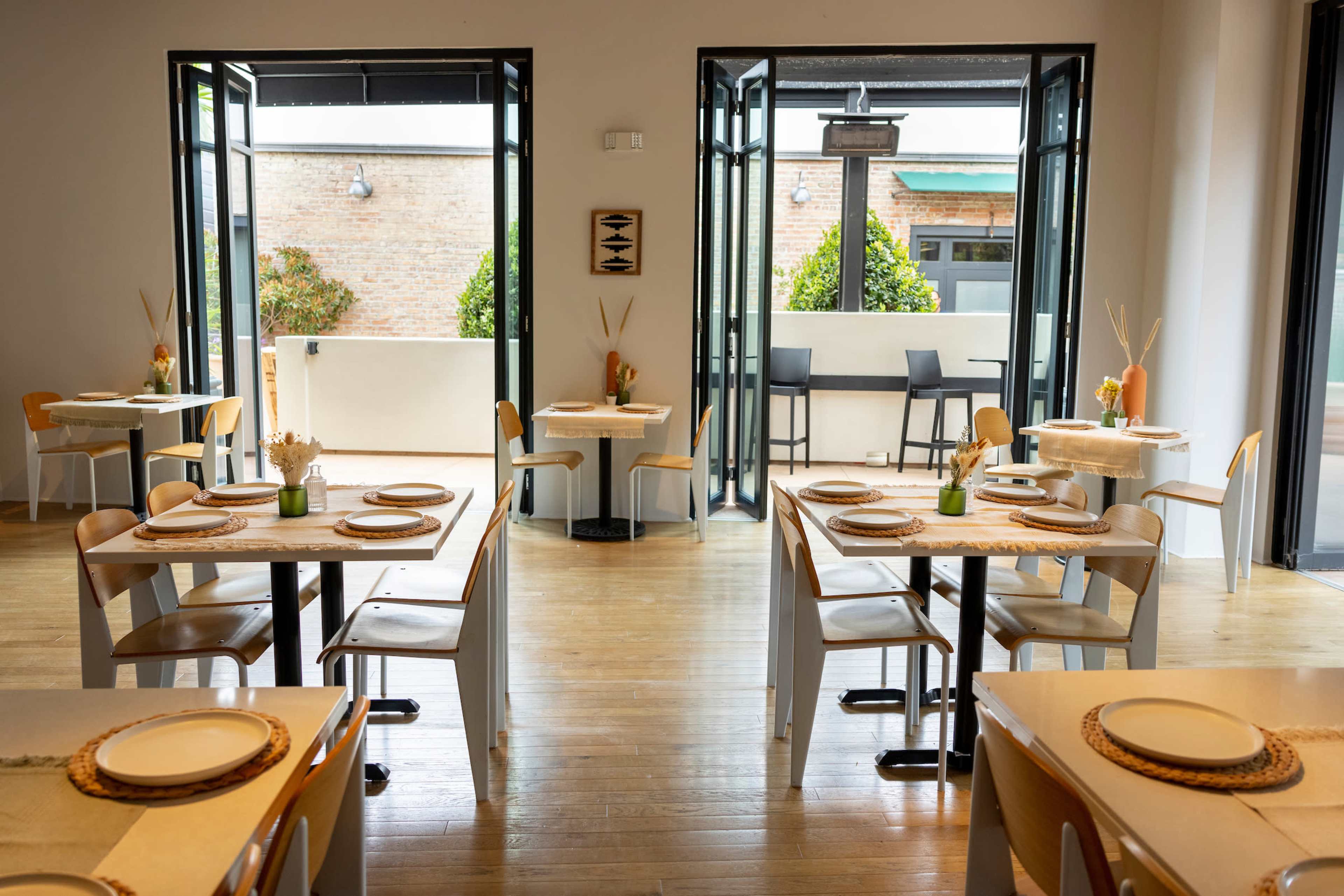 A spacious indoor dining area with tables set for meals, large open doors leading to an outdoor space, and a minimalist decor style.