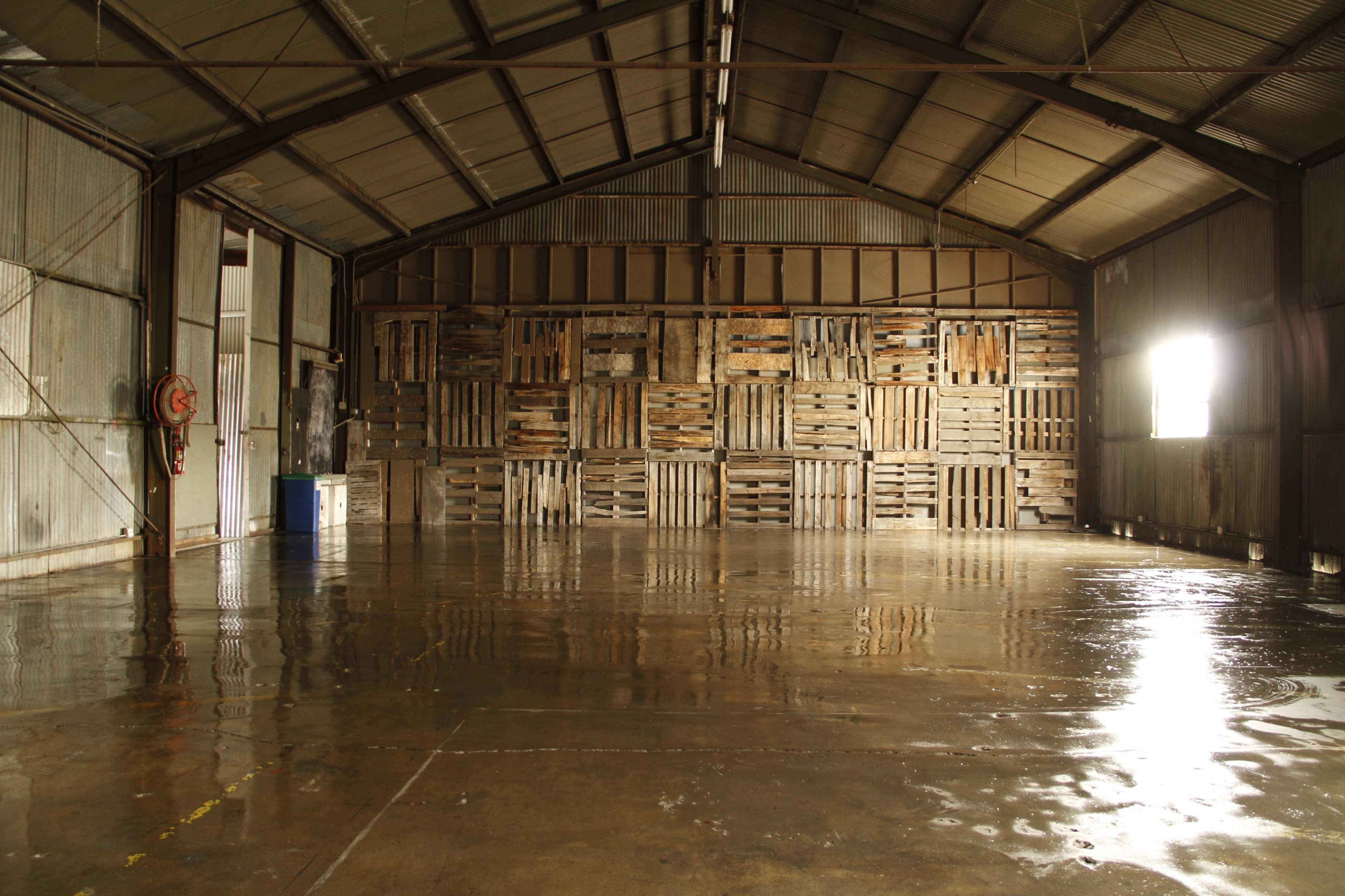 The image shows an empty warehouse interior with a polished concrete floor and wooden pallets stacked against one wall.