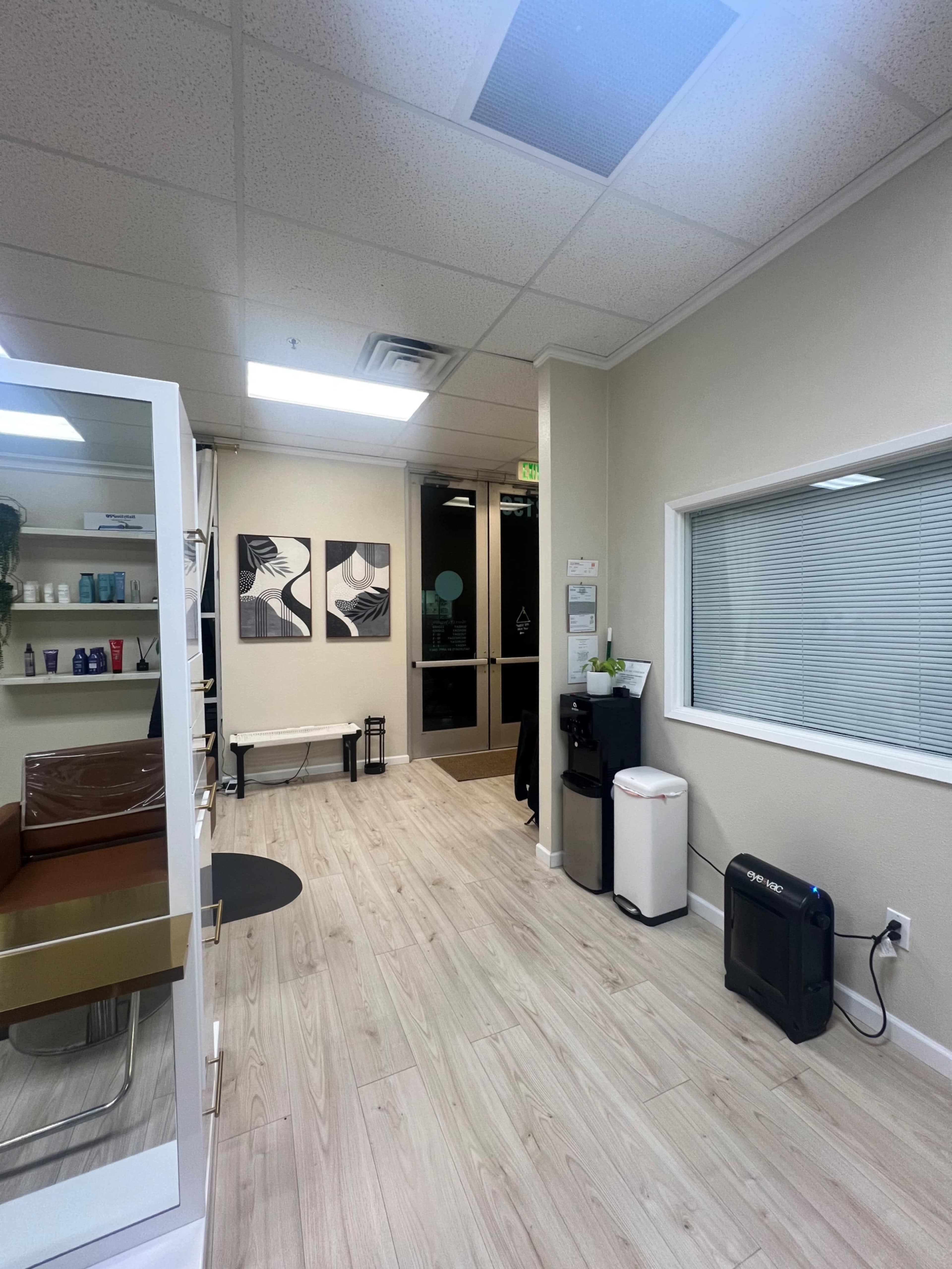 A well-lit hallway in a clinic or salon, featuring wooden flooring, wall art, and reception furniture.