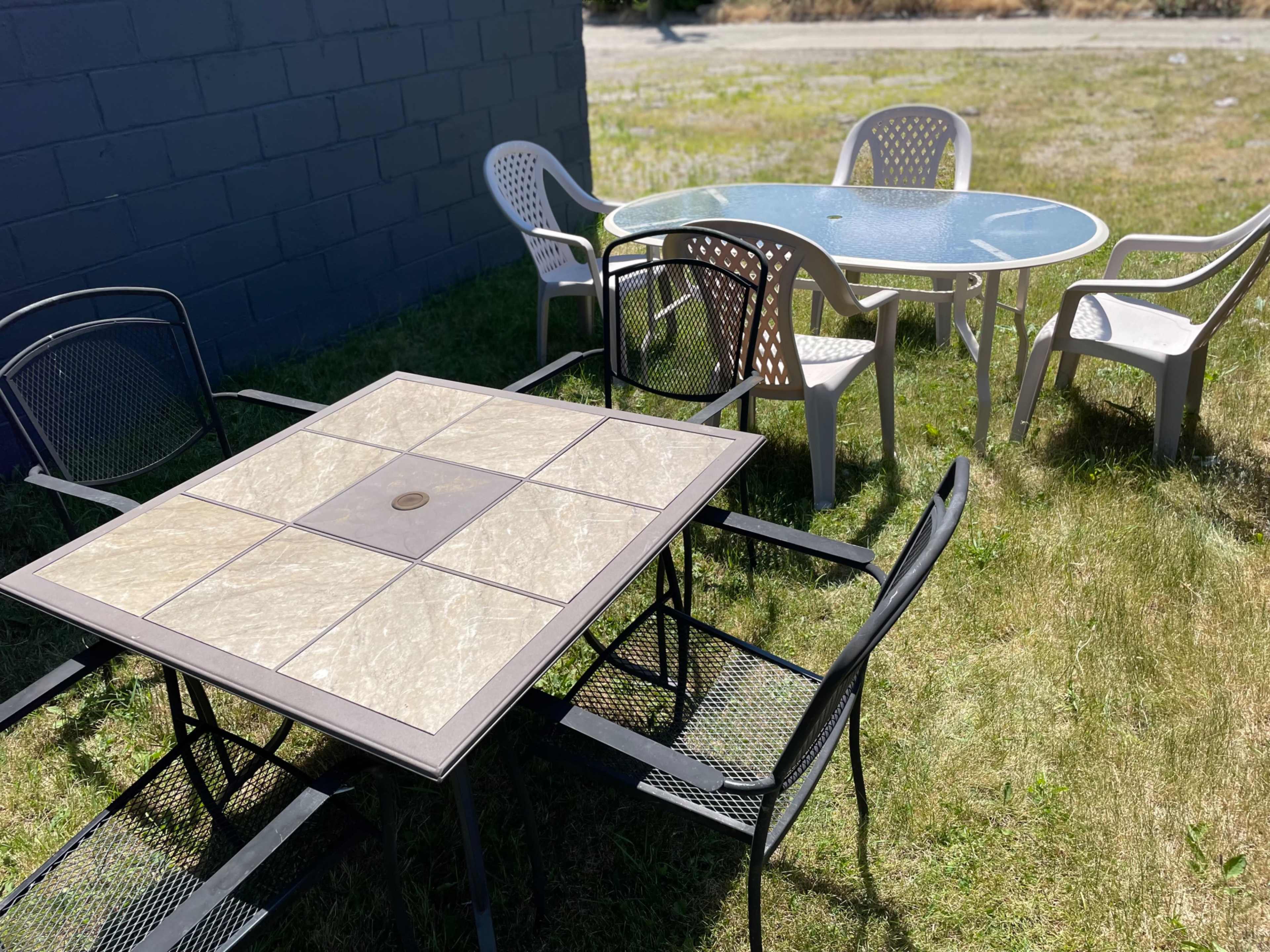 A set of outdoor tables and chairs sits on a grassy area beside a gray wall.