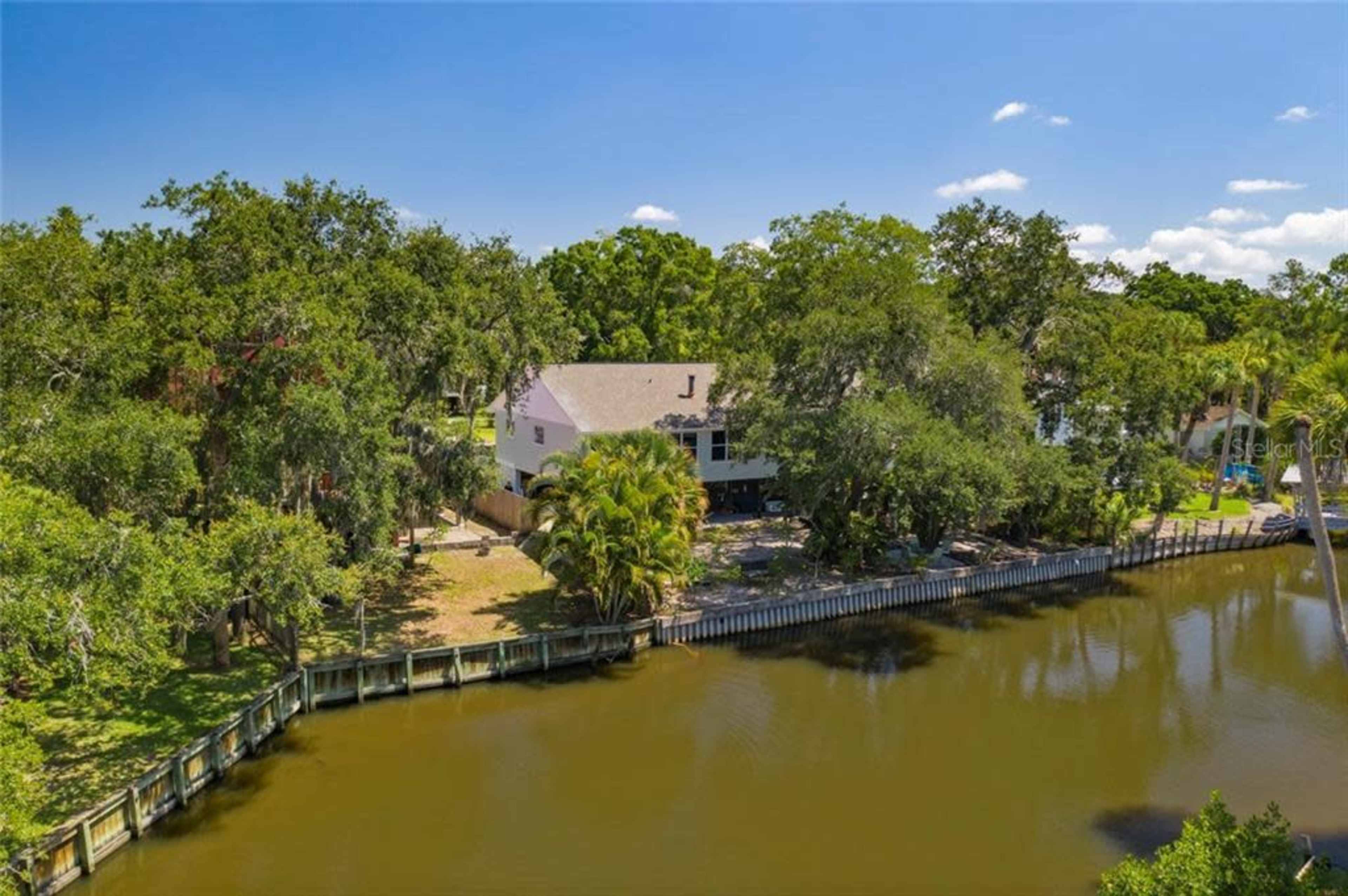 A residential area with a house surrounded by trees near a calm waterway and a wooden dock.