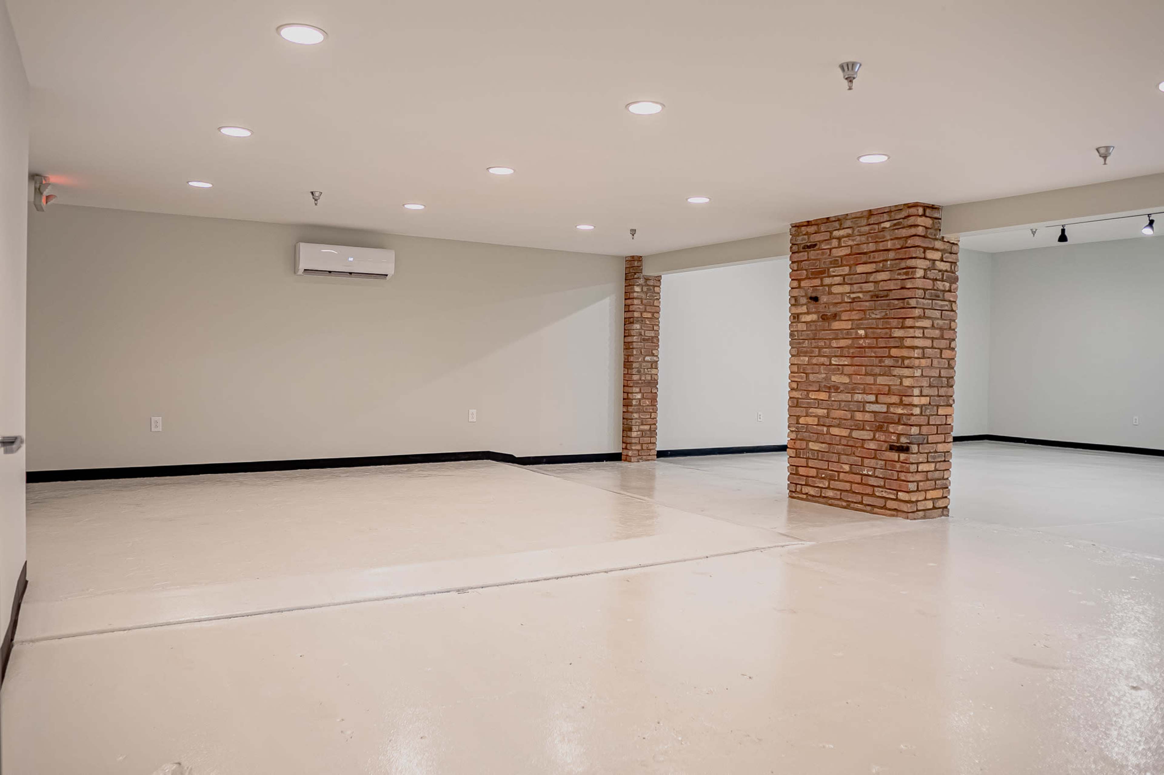 A large, empty room with a polished white floor, light-colored walls, and a brick column near the center.