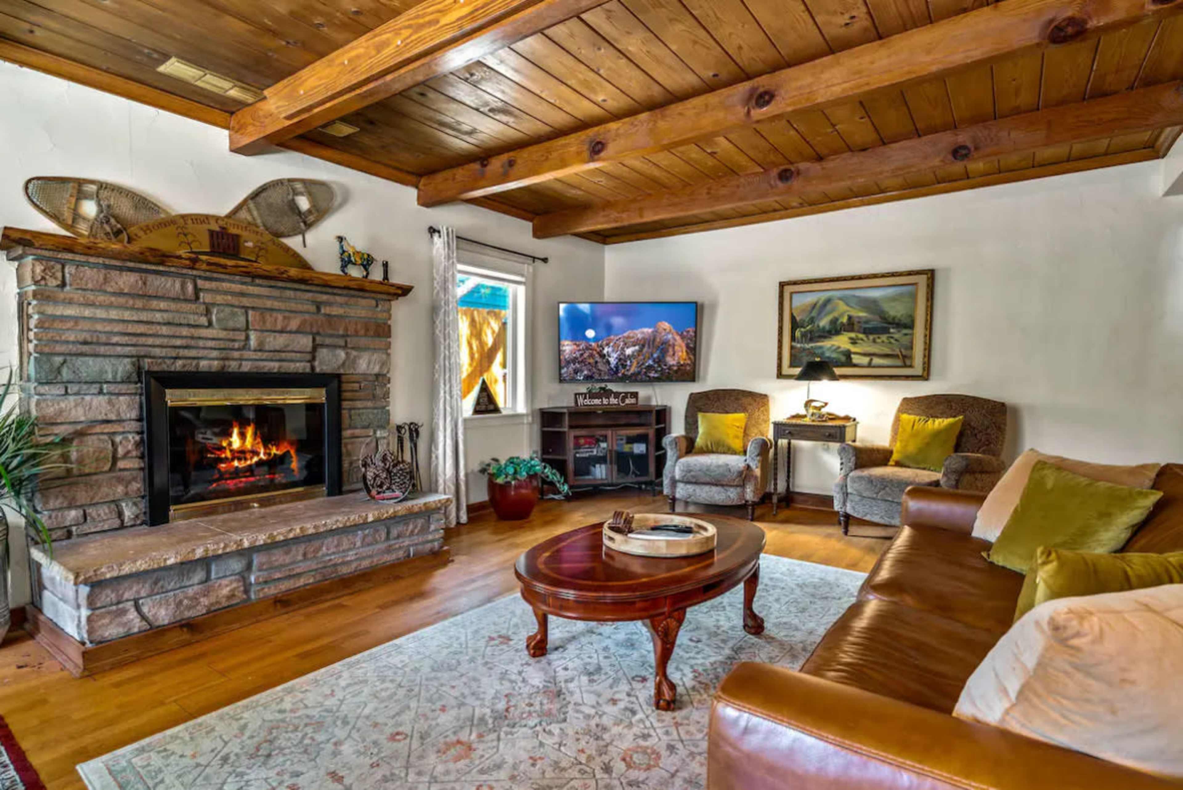 The room features a stone fireplace, a wooden ceiling, a leather couch, and two upholstered chairs, creating a cozy living space.