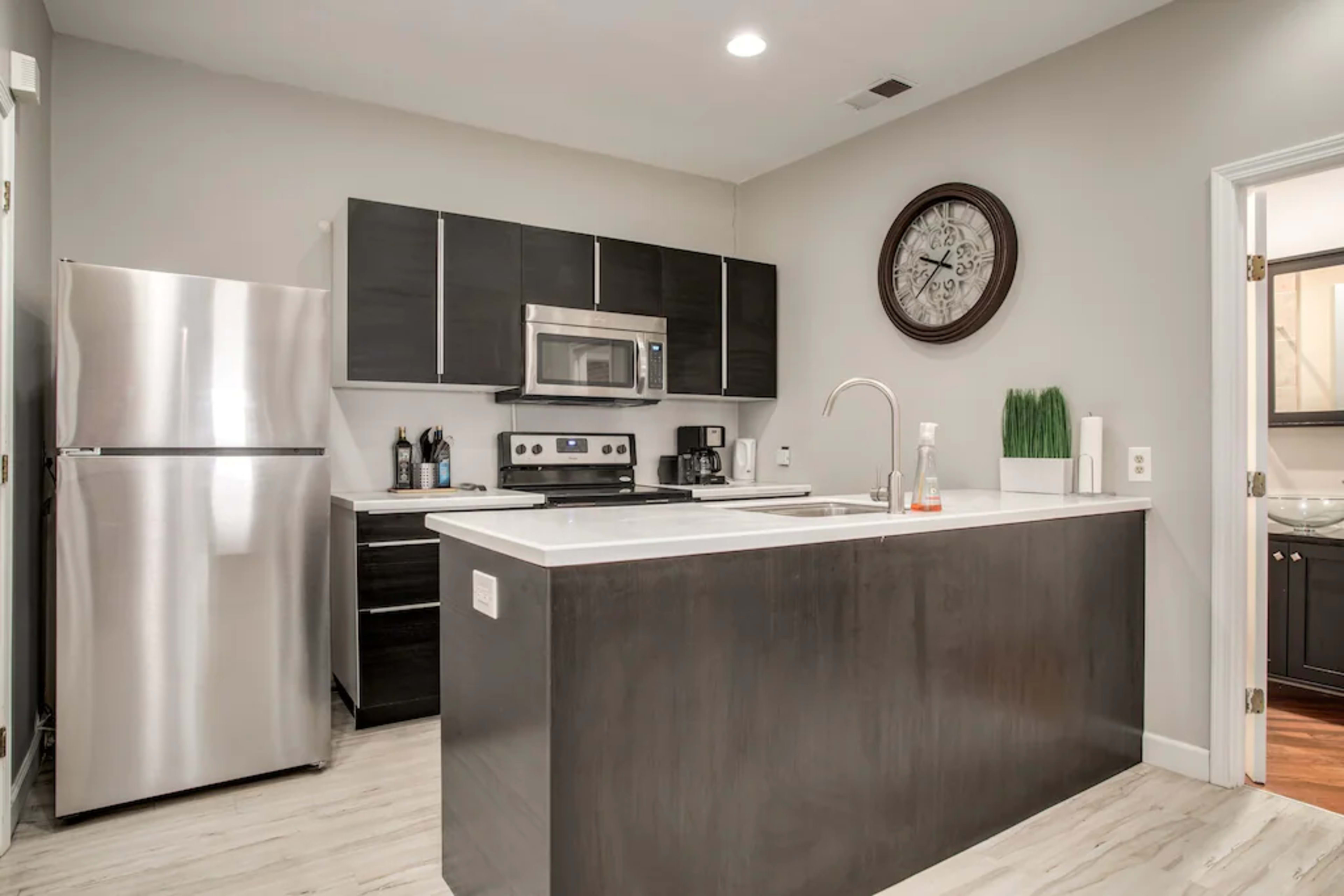 A modern kitchen with dark cabinetry, stainless steel appliances, and a central island with a sink.
