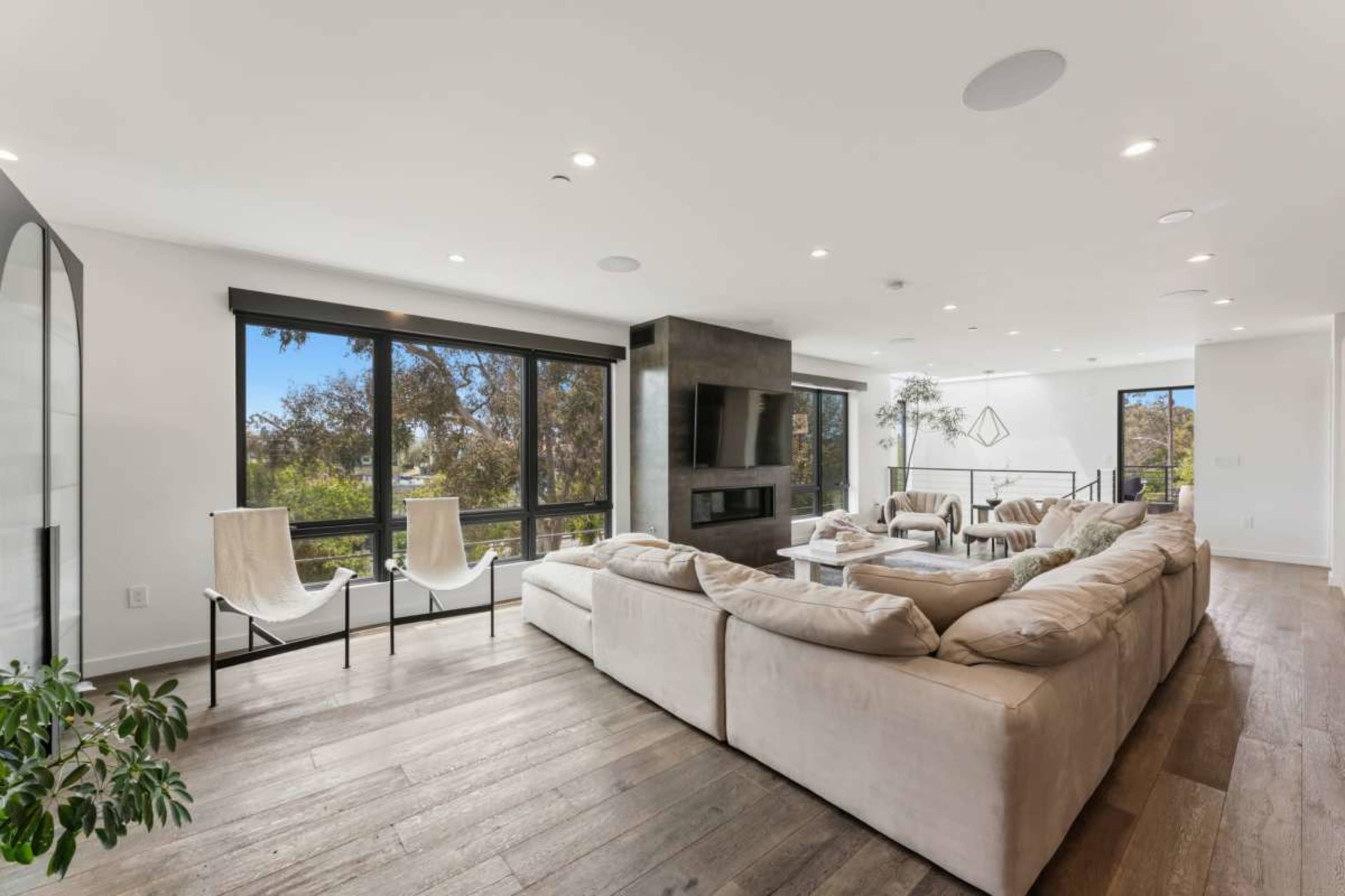 The image shows a modern living room with large windows, a sectional sofa, and minimalistic decor.