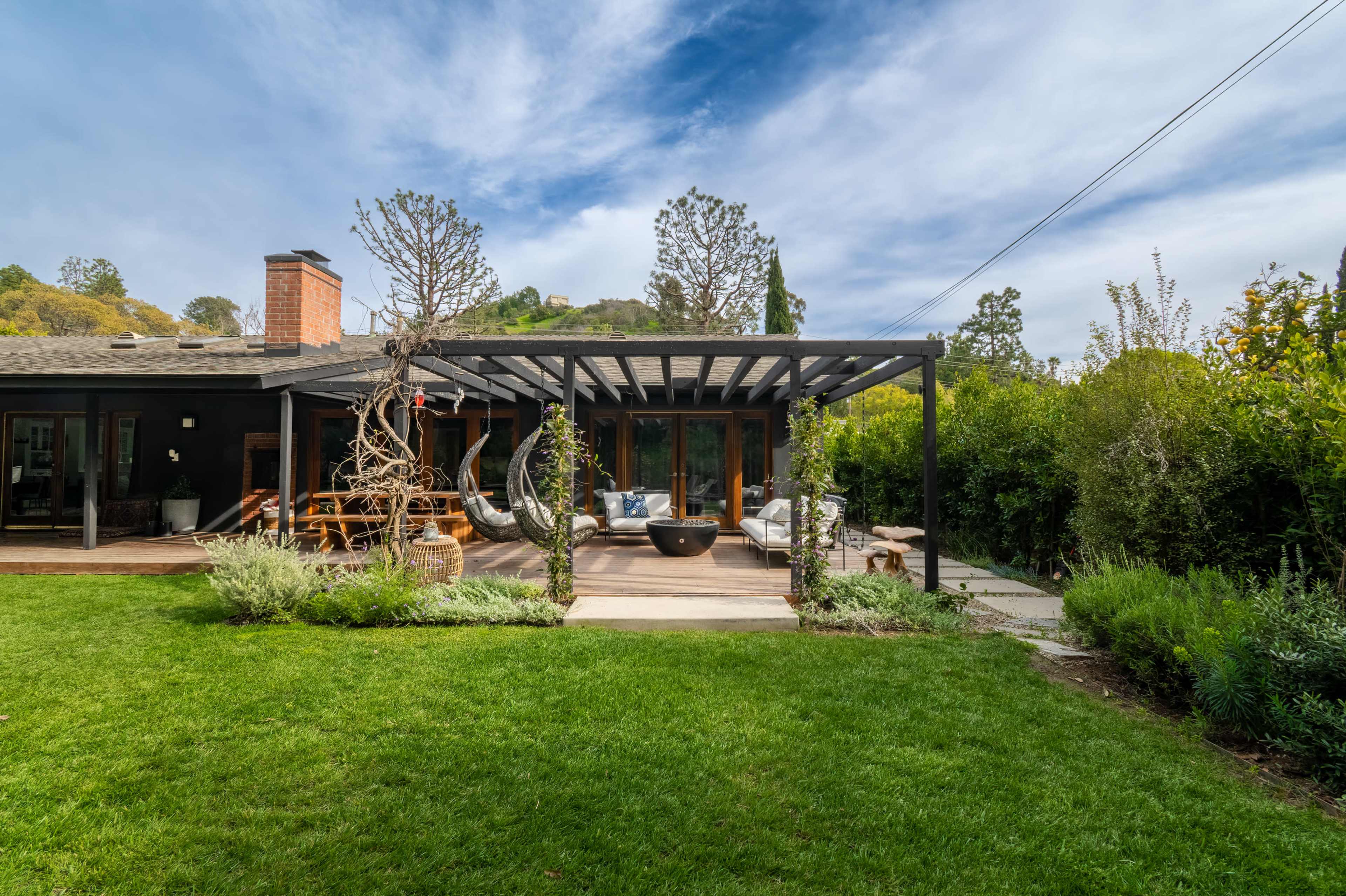 A modern house features a patio with outdoor seating, surrounded by lush greenery and trees.