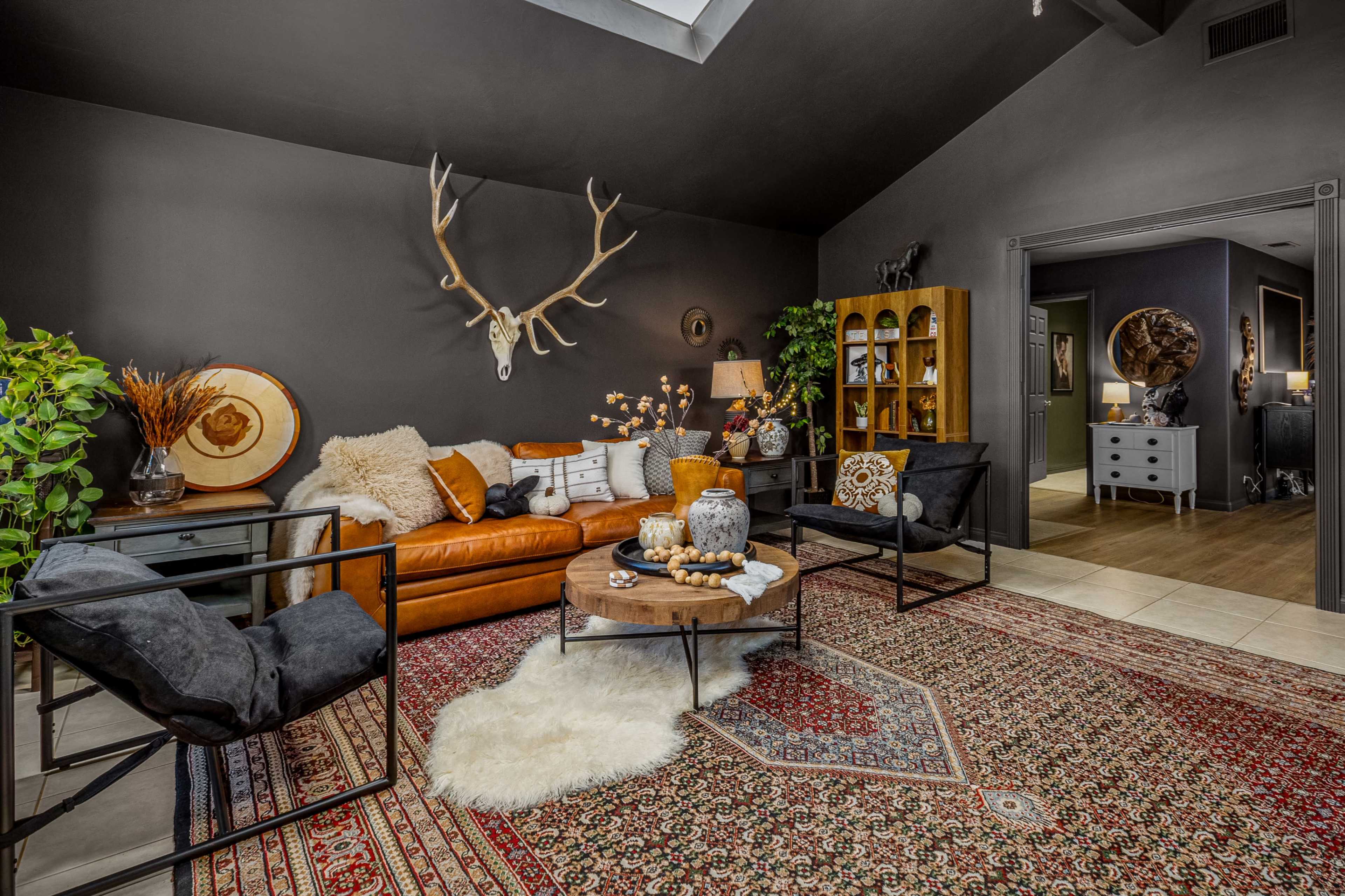 The living room features a dark wall with an antler mount, a brown leather sofa, a round coffee table, and decorative plants, creating a cozy and inviting atmosphere.