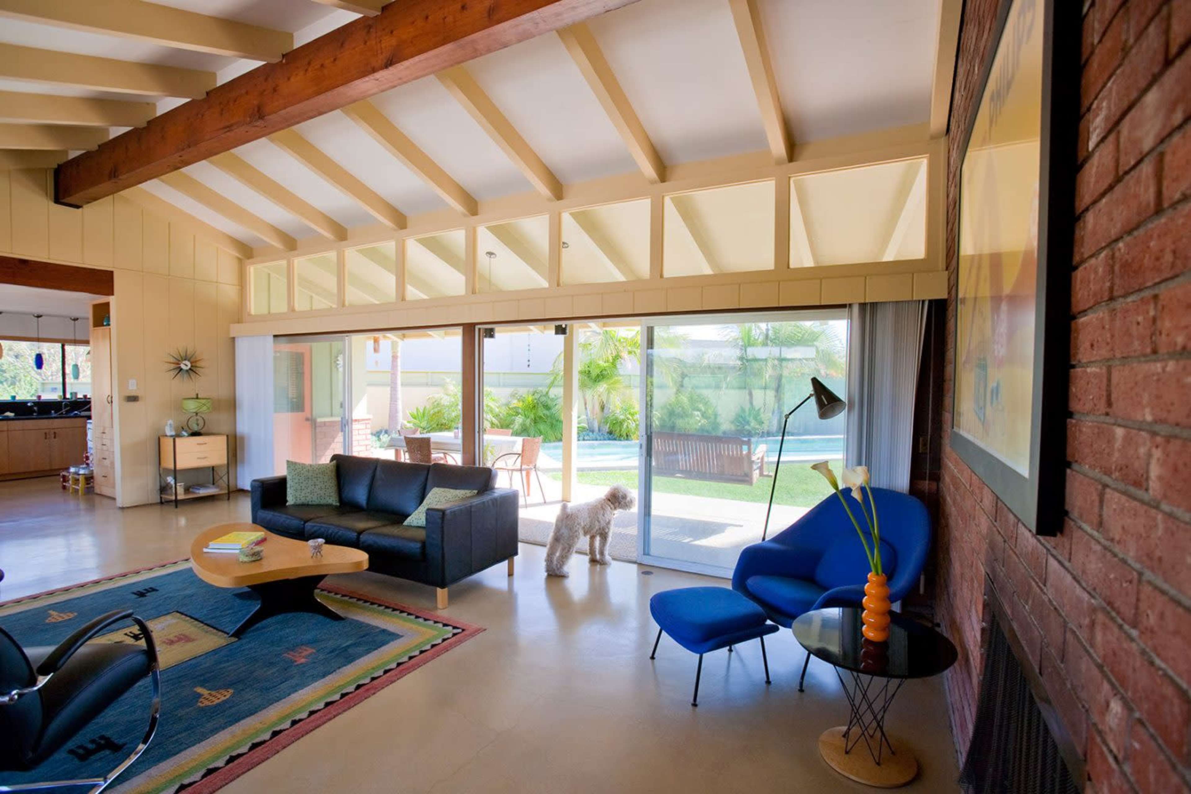 A spacious living room features a sofa, blue chairs, and large glass doors leading to a patio with outdoor seating.