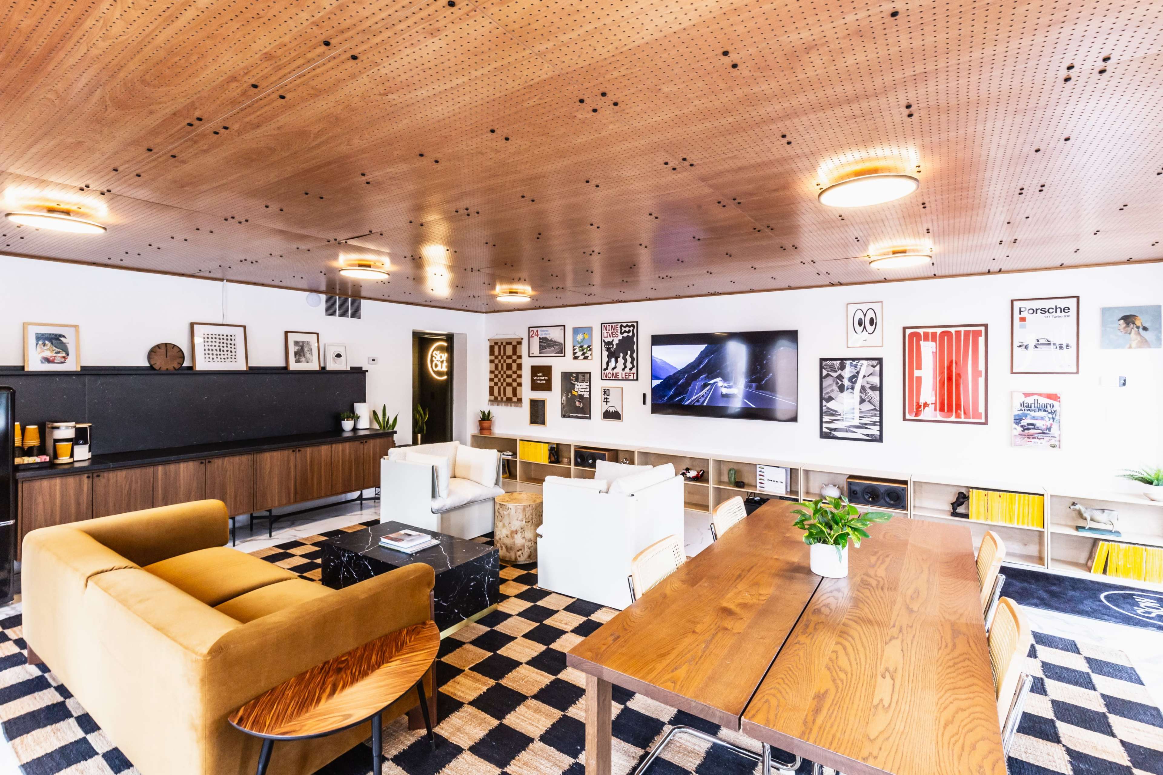 A modern lounge area featuring a seating arrangement with a sofa and chairs, a large wall-mounted television, a dining table, and various framed artworks on the walls.
