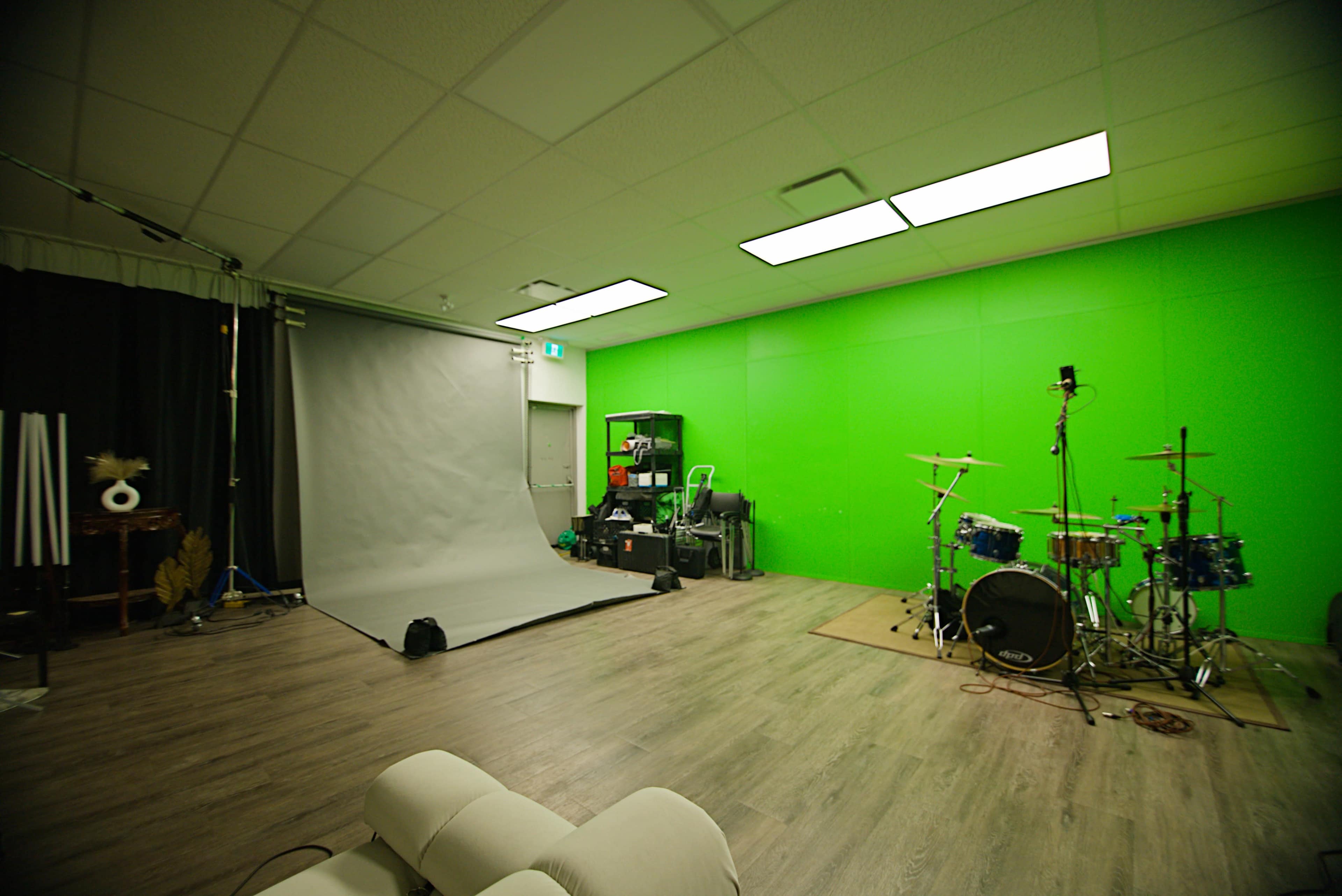 The image shows a studio space with a gray backdrop, green walls, a drum set, and various equipment arranged along one side.