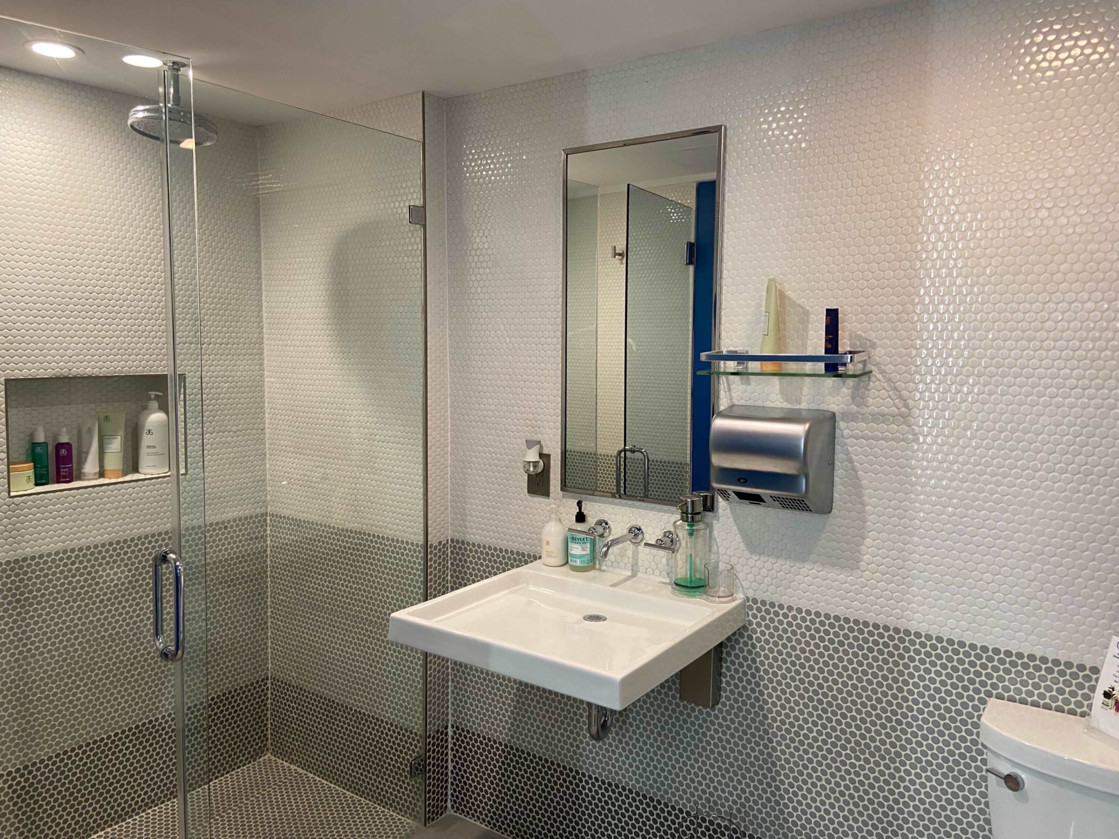 A modern bathroom with a hexagonal tiled wall, a glass shower enclosure, a rectangular mirror above a sink, and a toilet in the corner.
