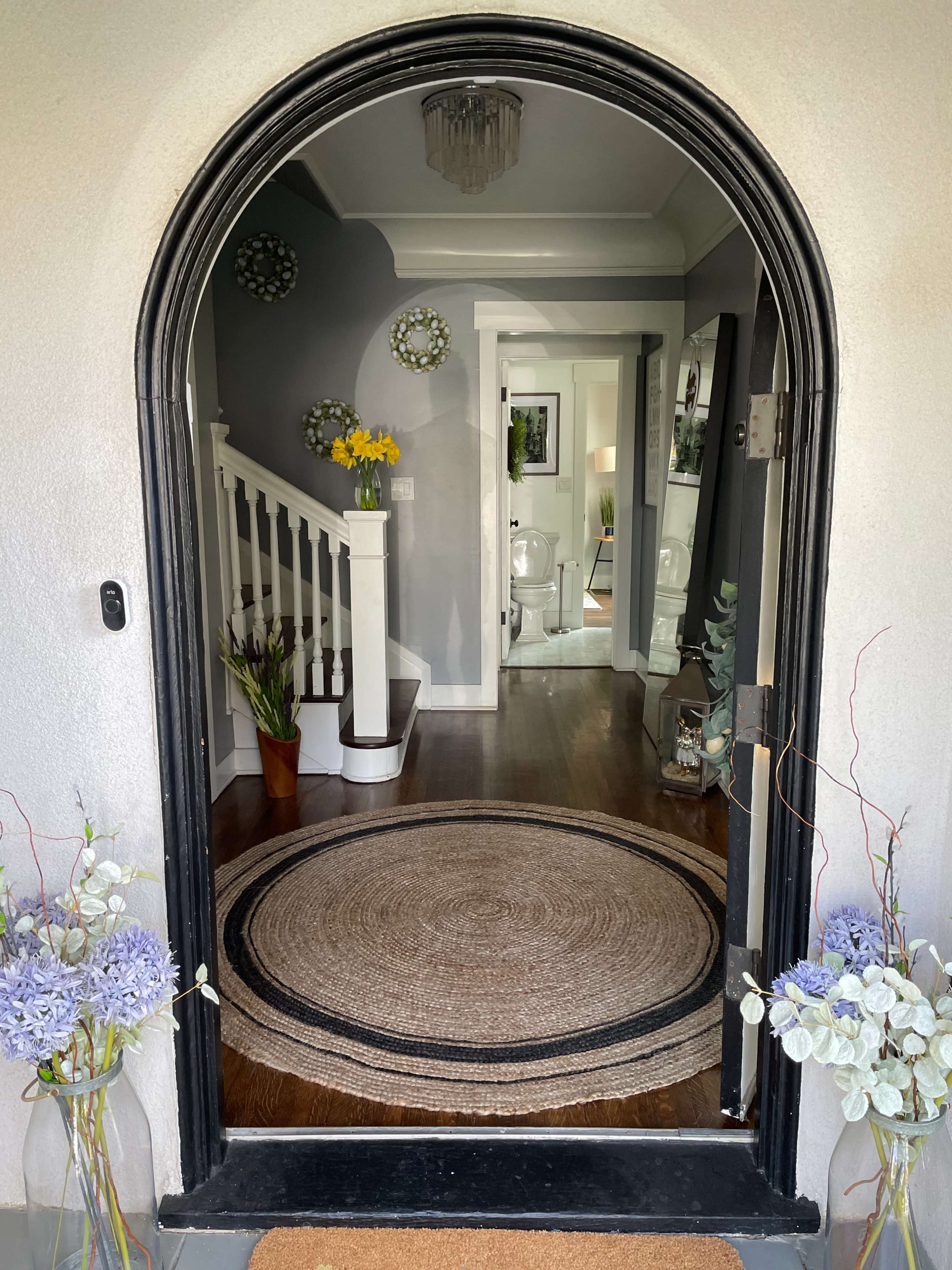 An arched doorway leading into a home with a round rug and decorative elements on either side, revealing a hallway and bathroom visible in the background.