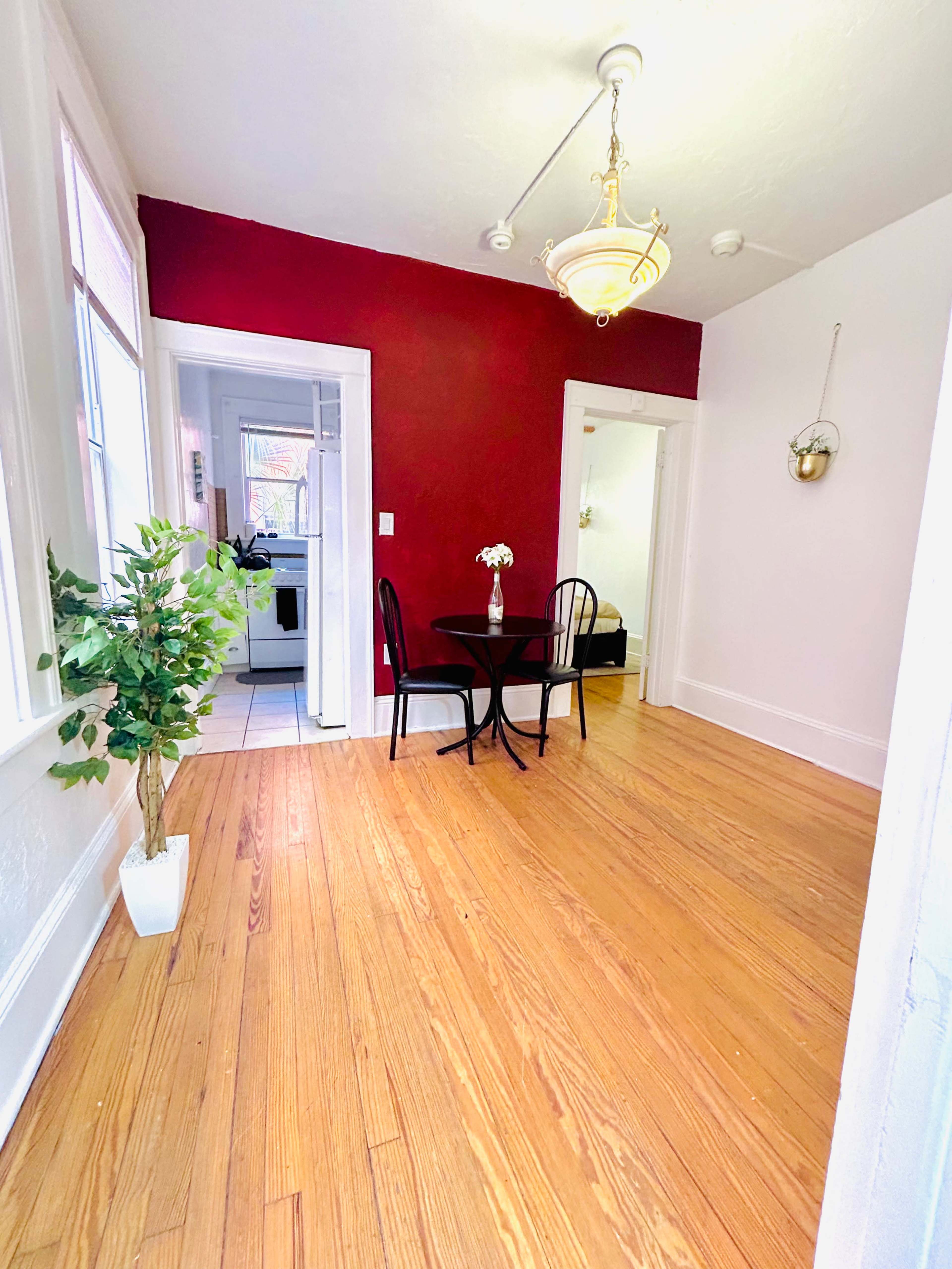 A bright room with hardwood floors, featuring a small round table and two chairs against a red accent wall.