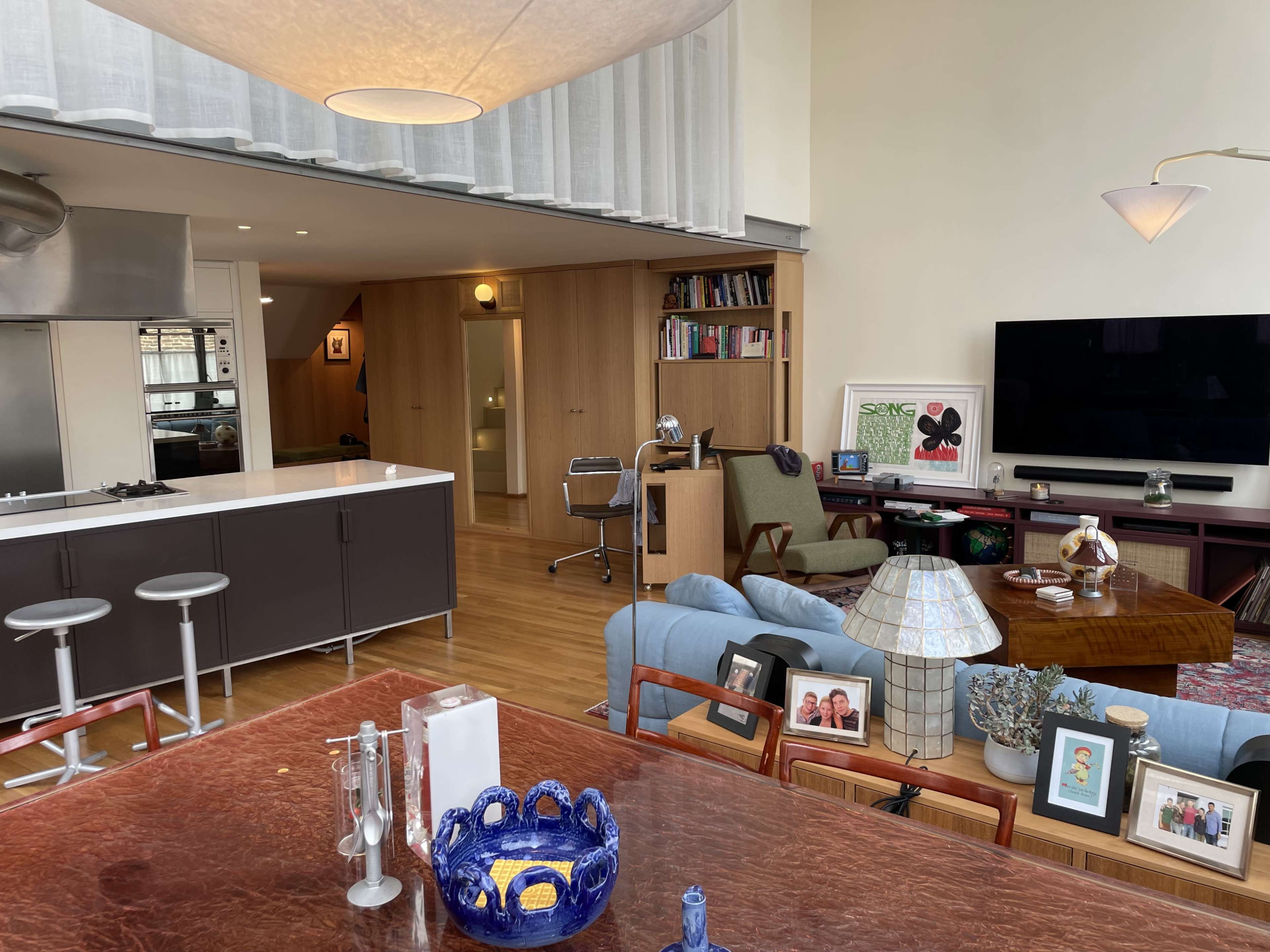 The image shows a modern living space featuring an open kitchen, a dining area with a large table, and a cozy seating area with various furnishings.