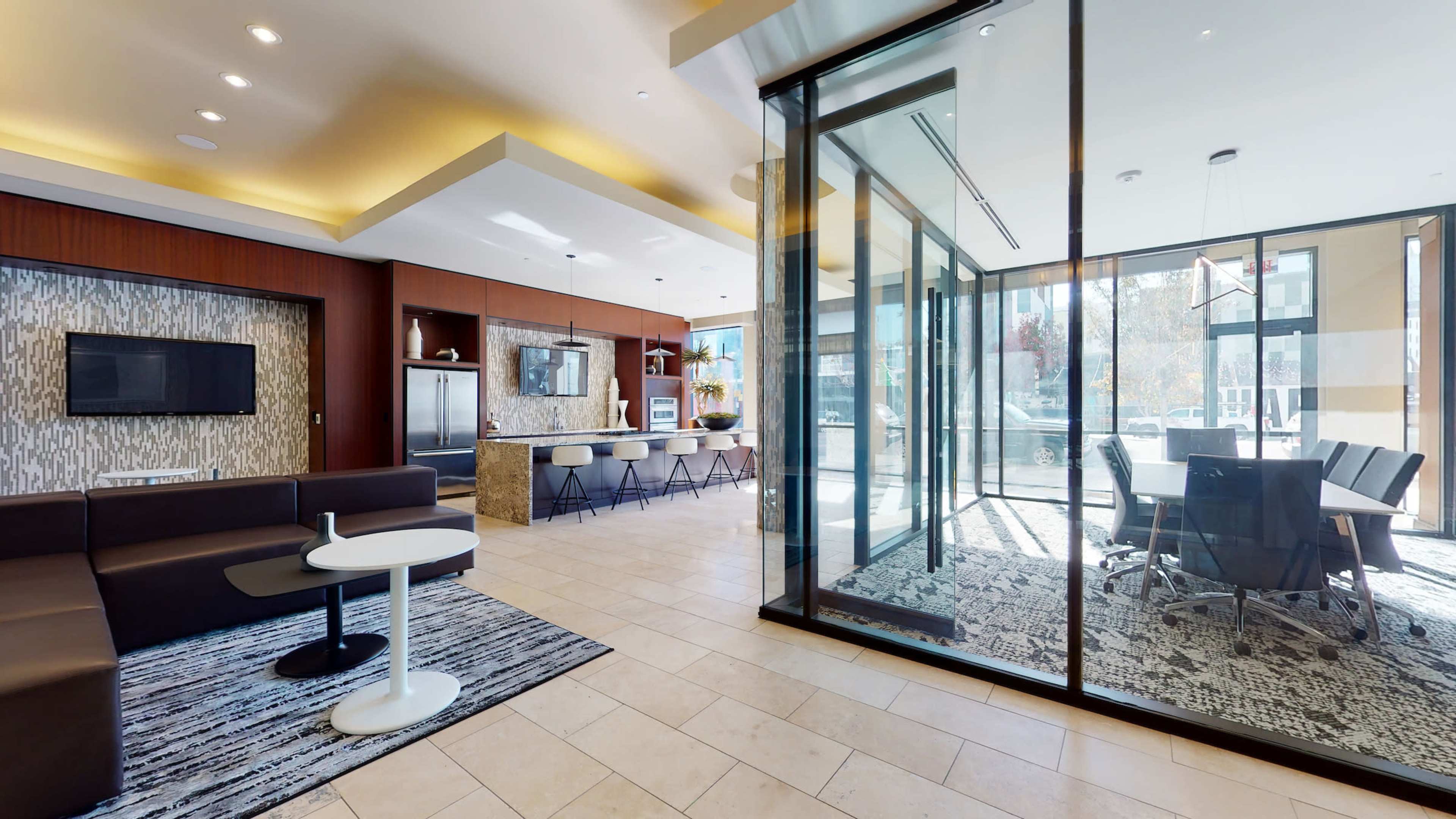 A modern lounge area with a seating arrangement, a kitchenette, and a glass-walled conference room.