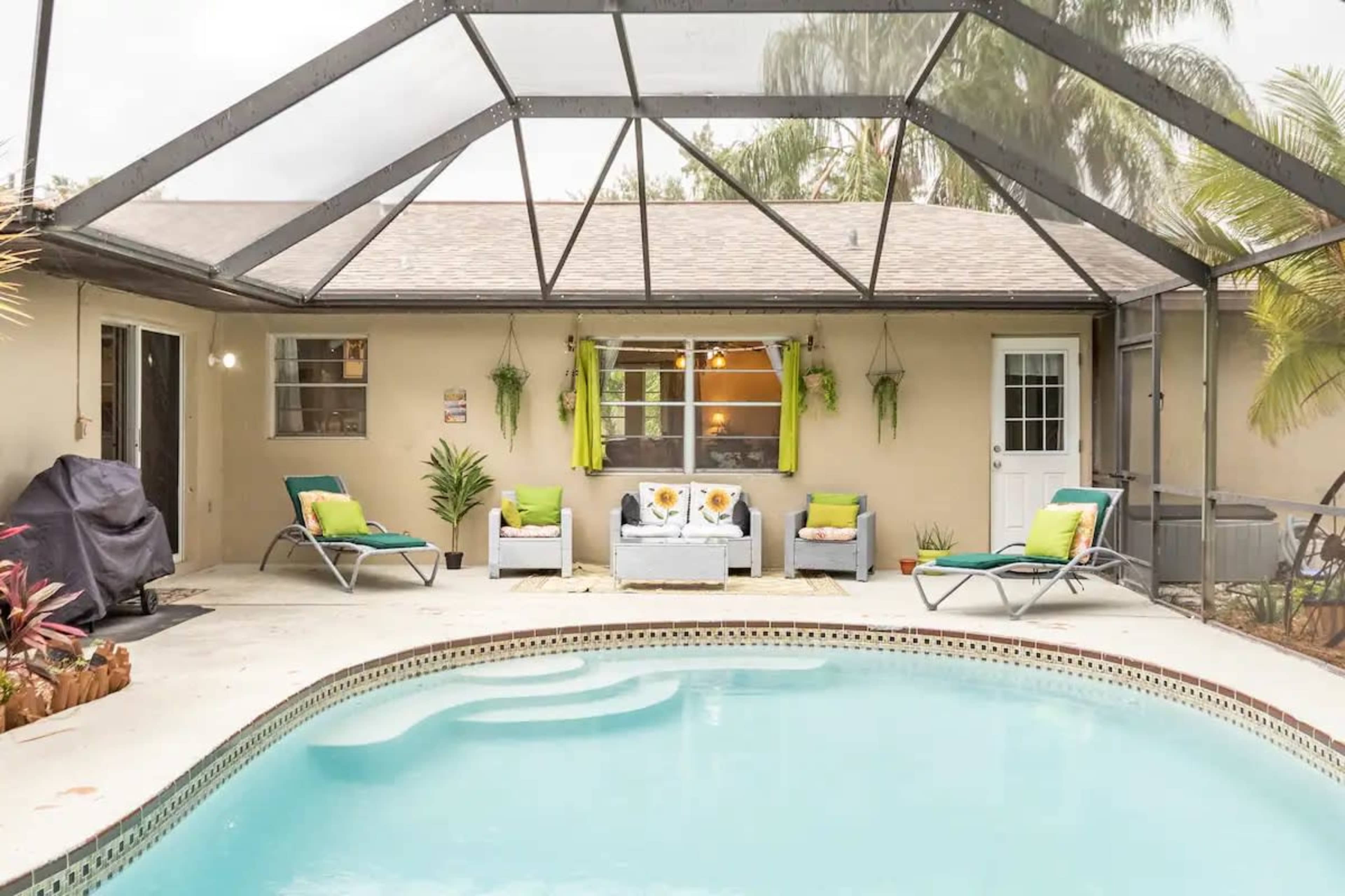 A screened patio features a swimming pool surrounded by lounge chairs and a seating area with vibrant cushions.