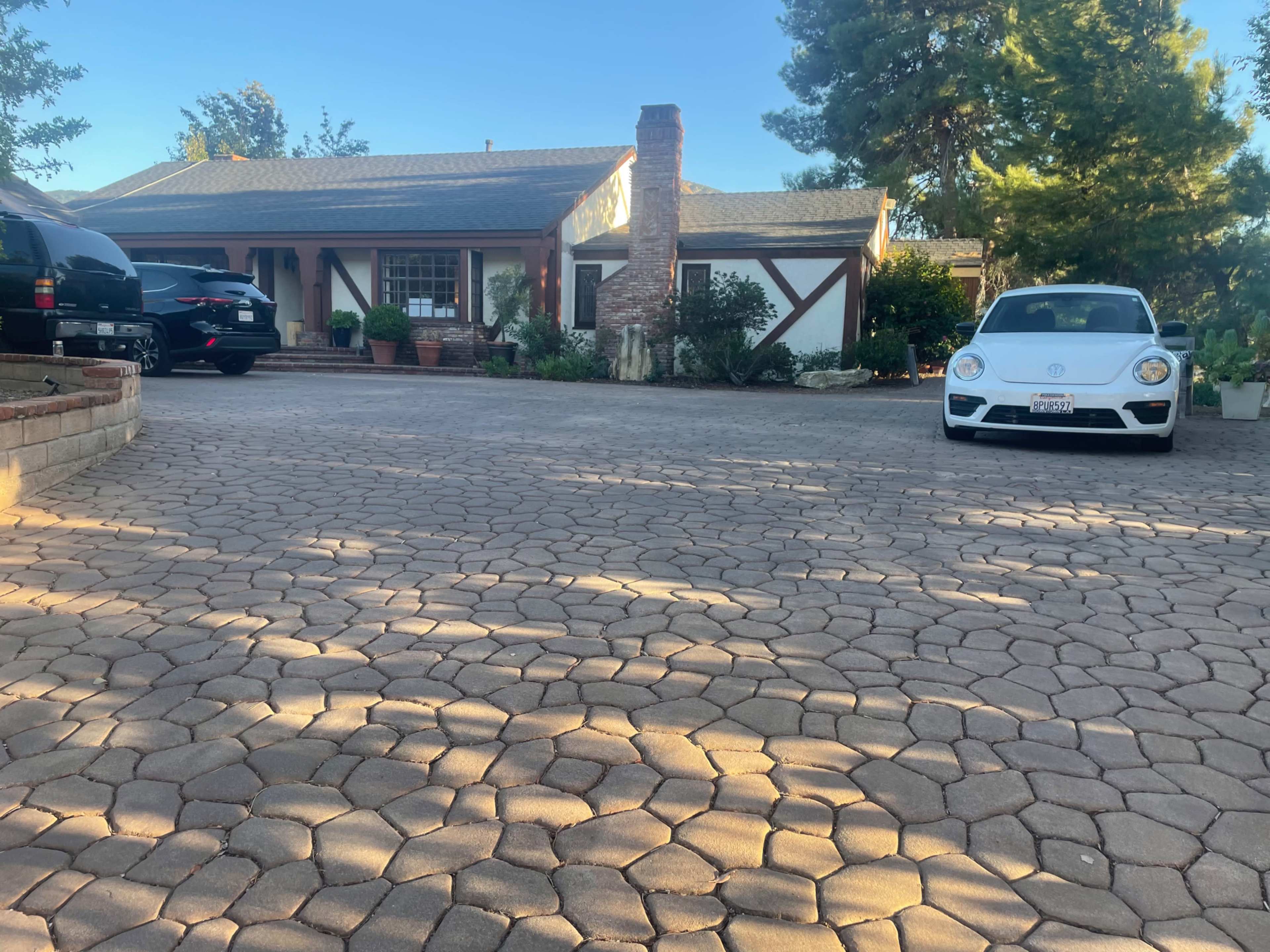 A residential home with a stone driveway features two parked cars and a garden in the front yard.