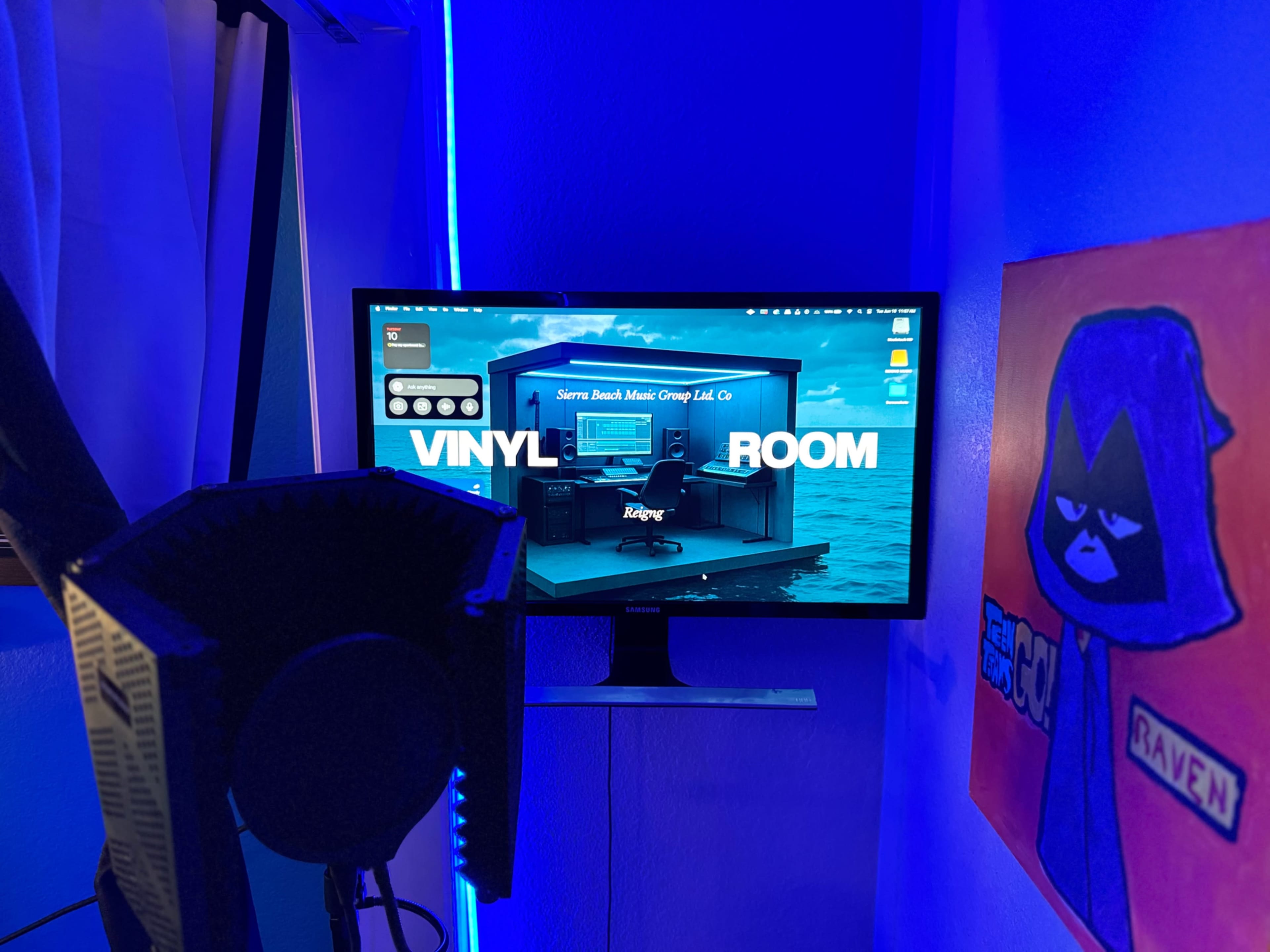 A computer monitor displays a vibrant graphic of a music studio setup labeled "VINYL ROOM," with ambient blue lighting and a colorful artwork on the wall nearby.