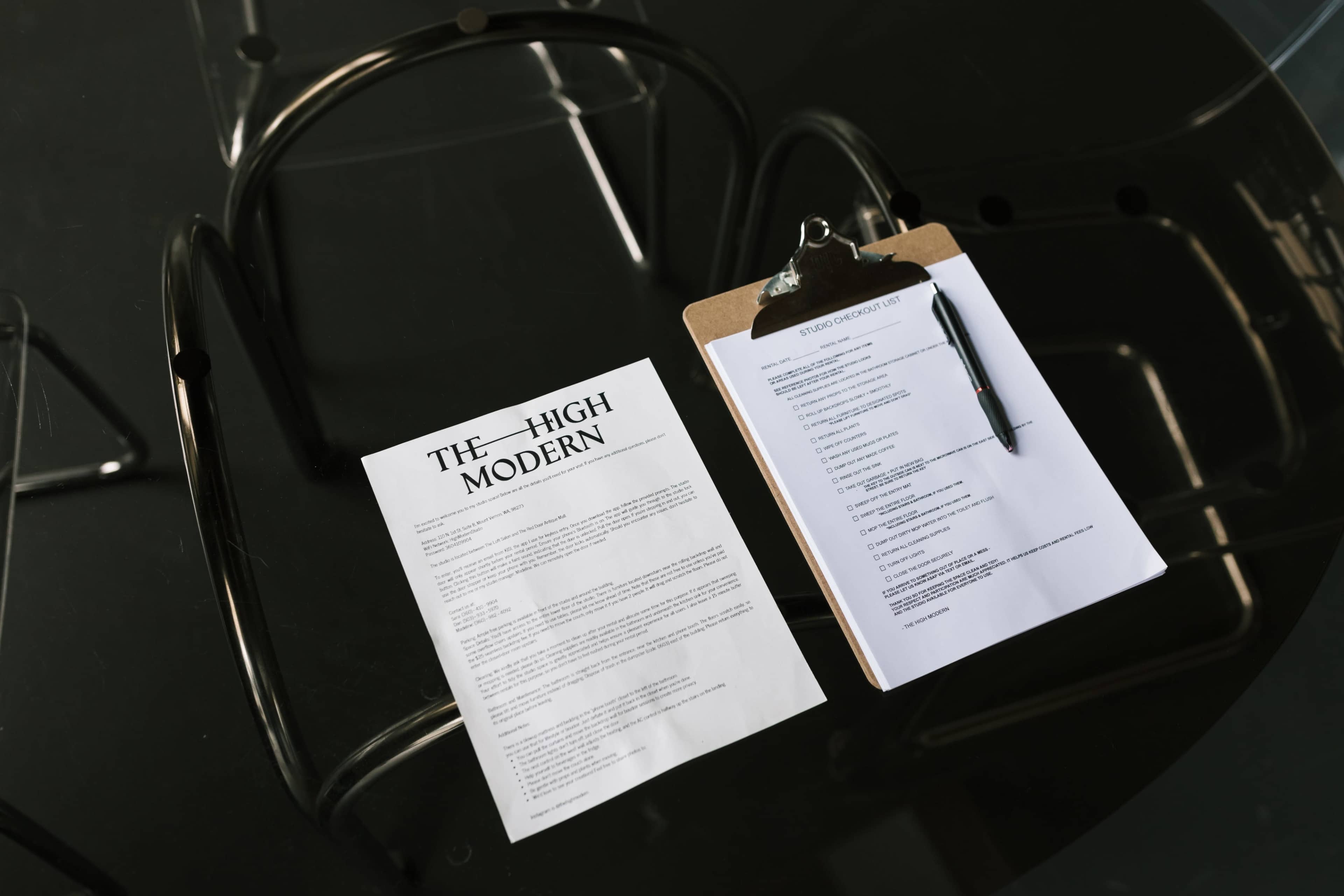 A sheet of paper titled "THE HIGH MODERN" and a clipboard with a pen rest on a dark, glossy table.