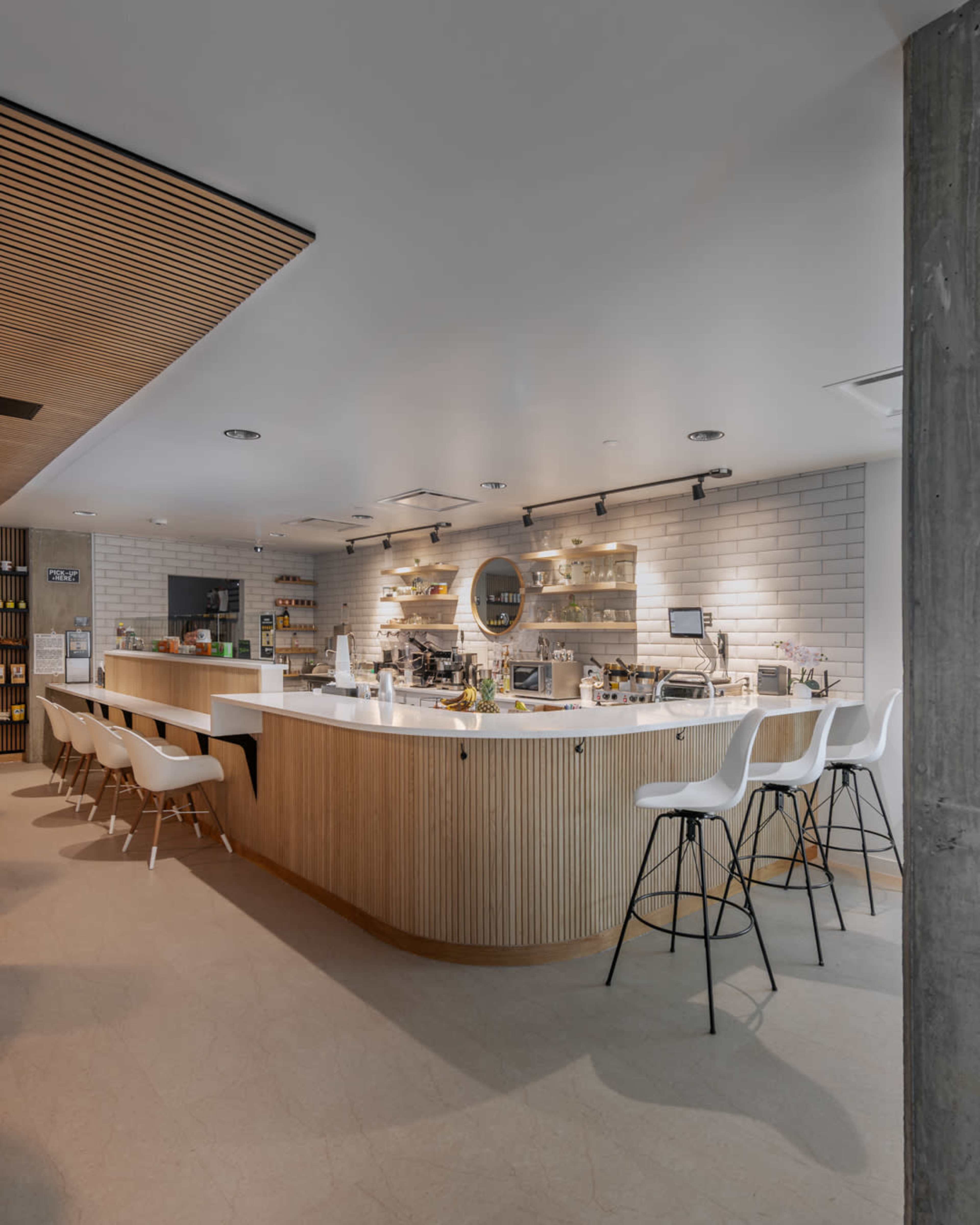 A modern café features a curved wooden counter with bar stools and a well-organized display of products in a bright, minimalist interior.