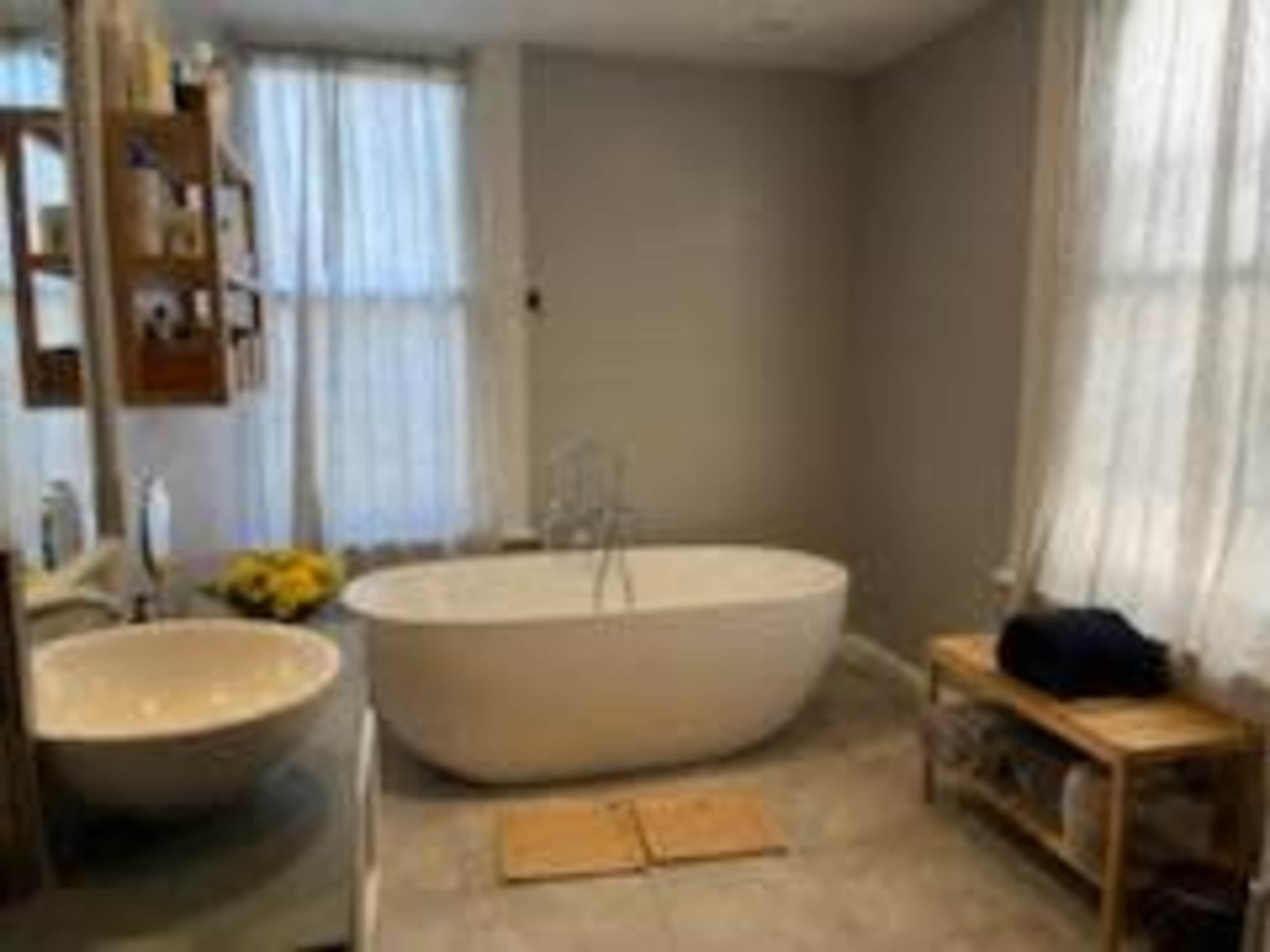 A spacious bathroom featuring a freestanding bathtub, a circular sink, and large windows with sheer curtains.