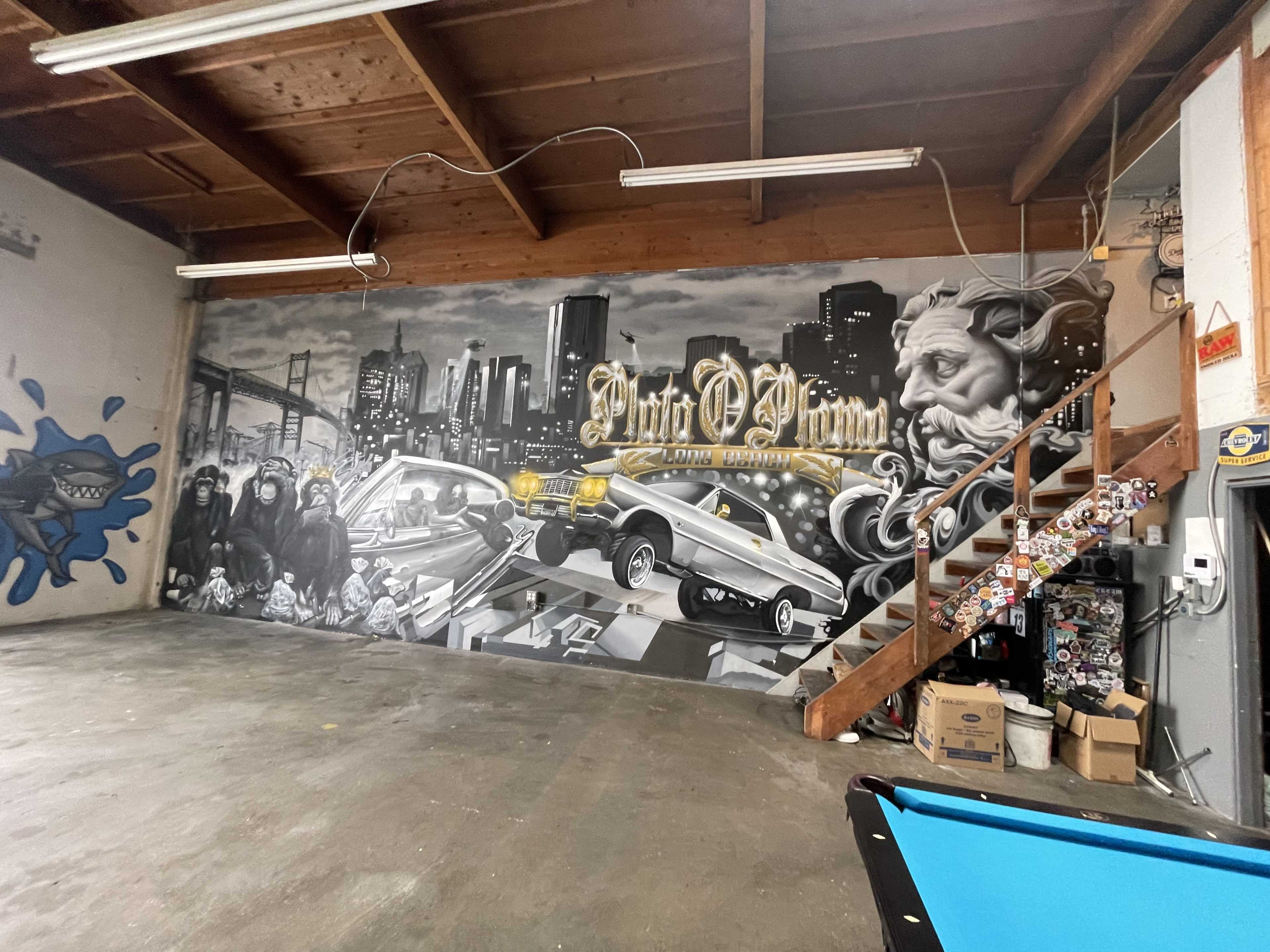 A spacious indoor area featuring a large mural depicting a cityscape along with classic cars and artistic figures, alongside a wooden staircase in the background.