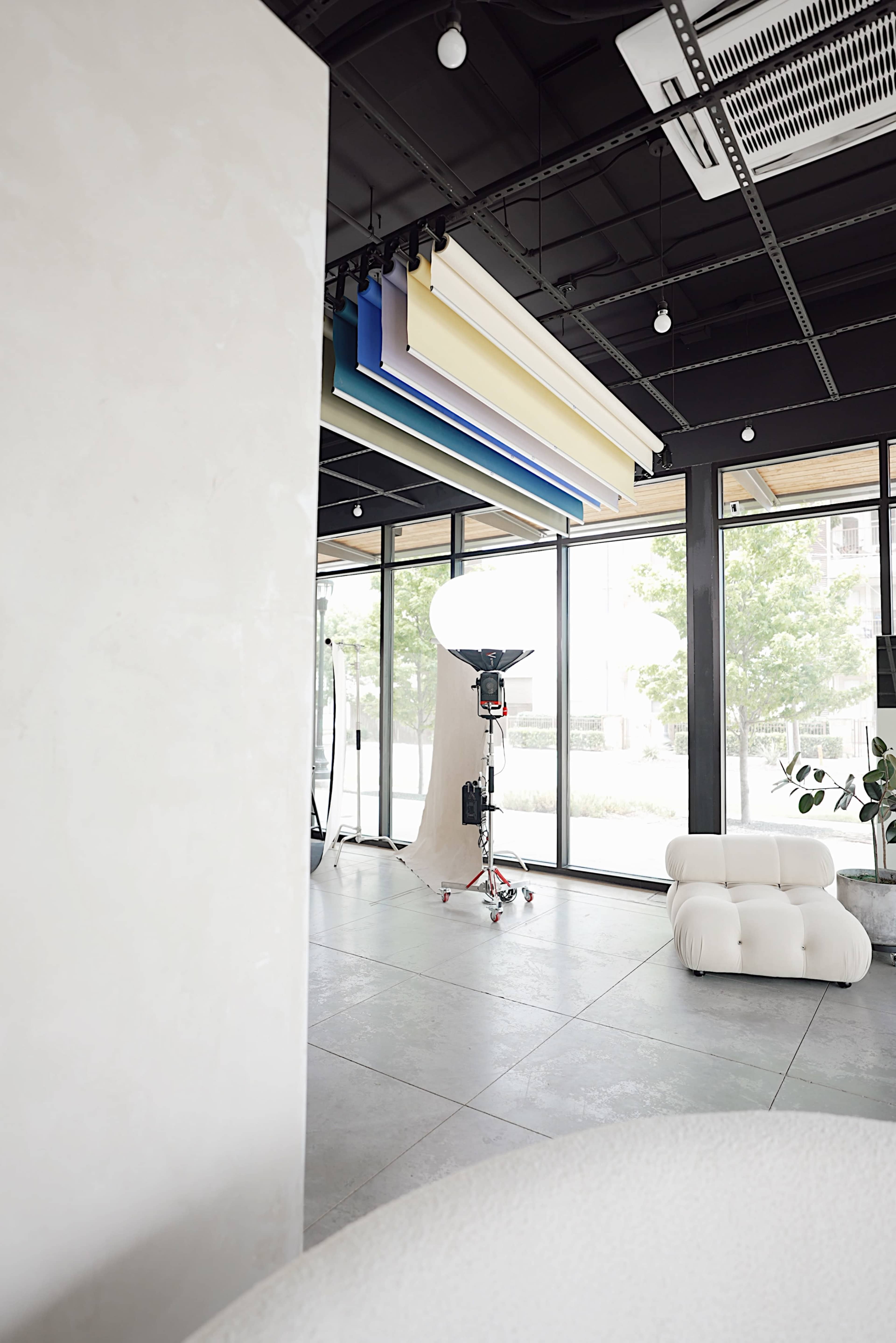 The interior features a modern, minimalistic design with large windows, a photography light setup, and colorful backdrop panels hanging from the ceiling.