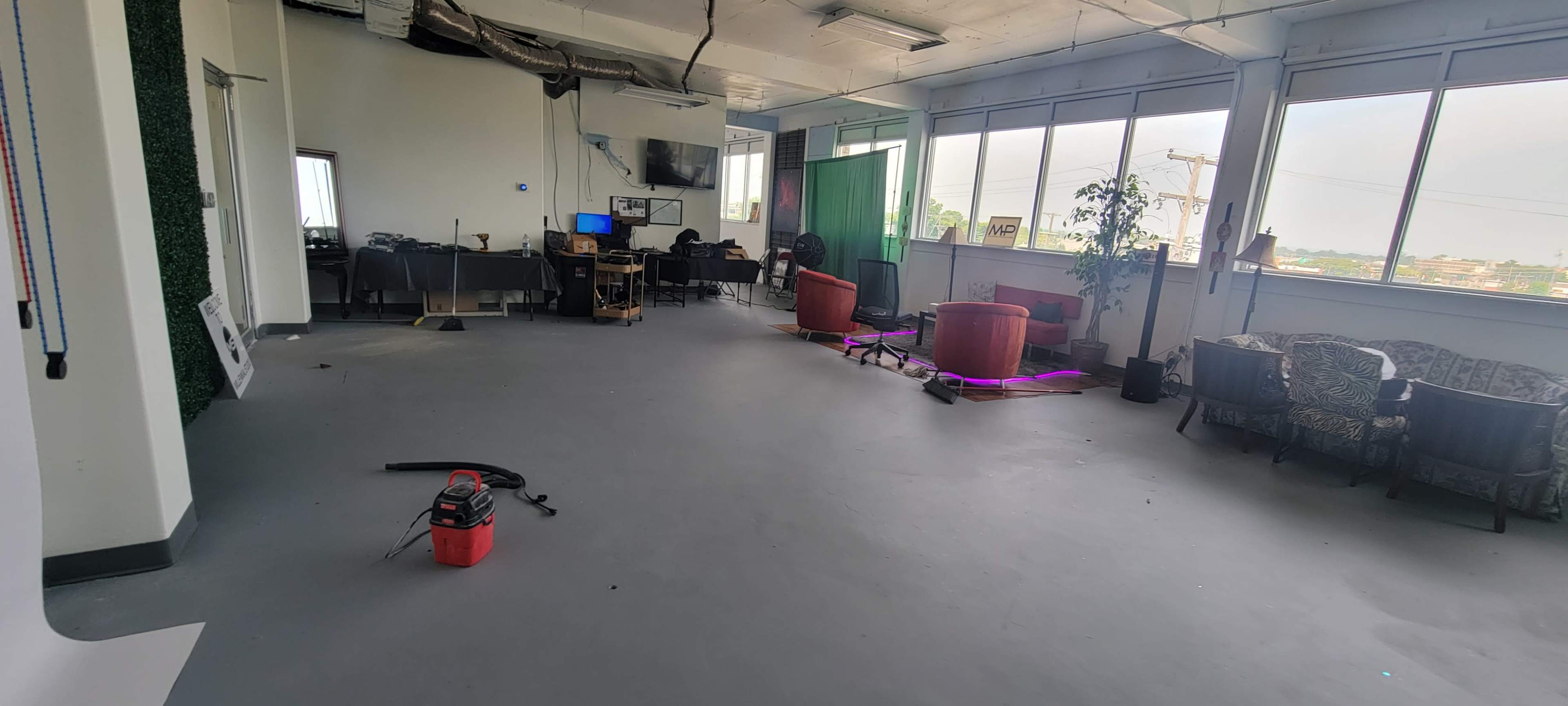 An empty office space with a few desks, chairs, and potted plants, along with some scattered equipment on the floor.