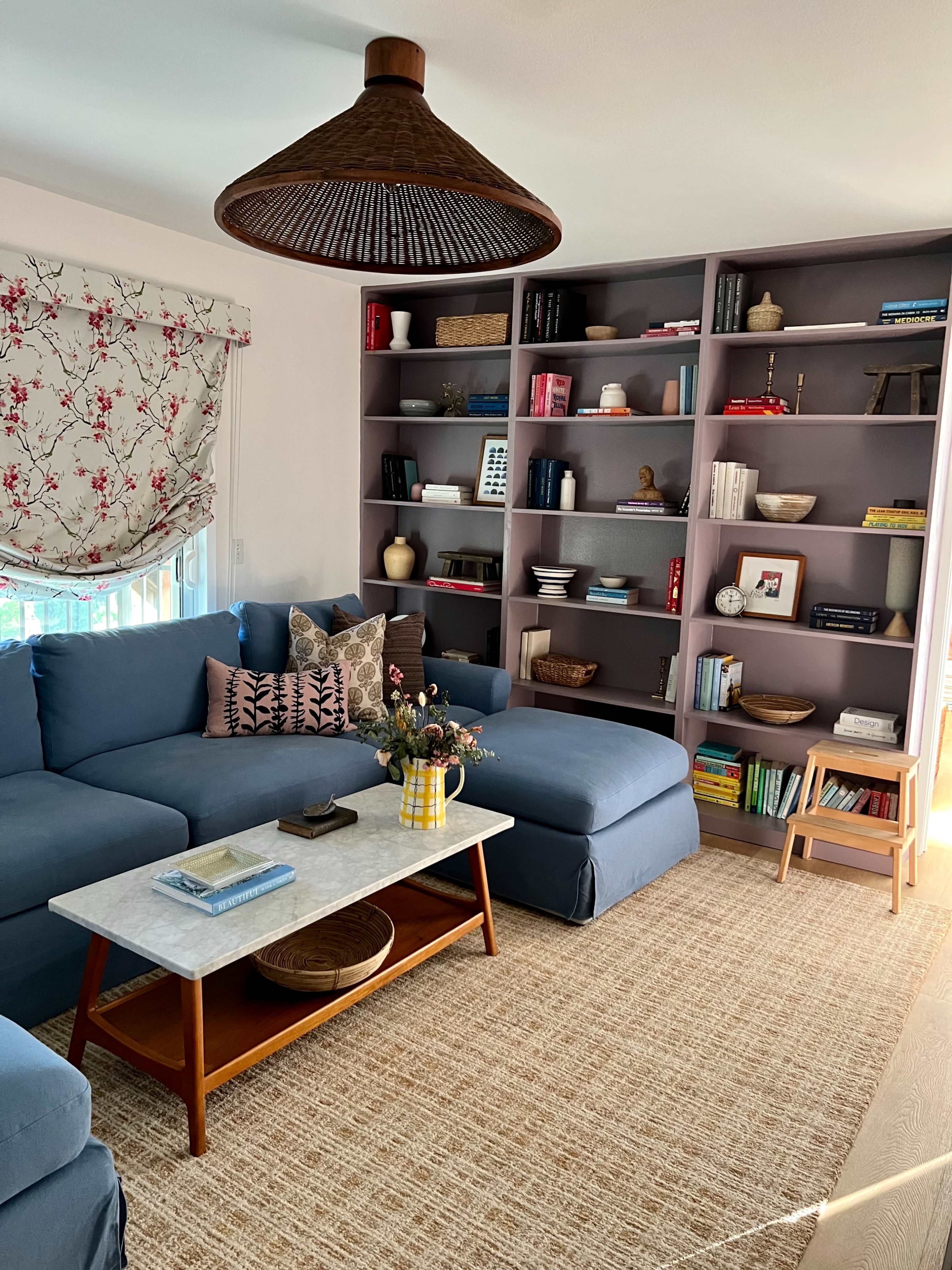 A cozy living room featuring a large blue sectional sofa, a marble coffee table, and shelving filled with books and decorative items.