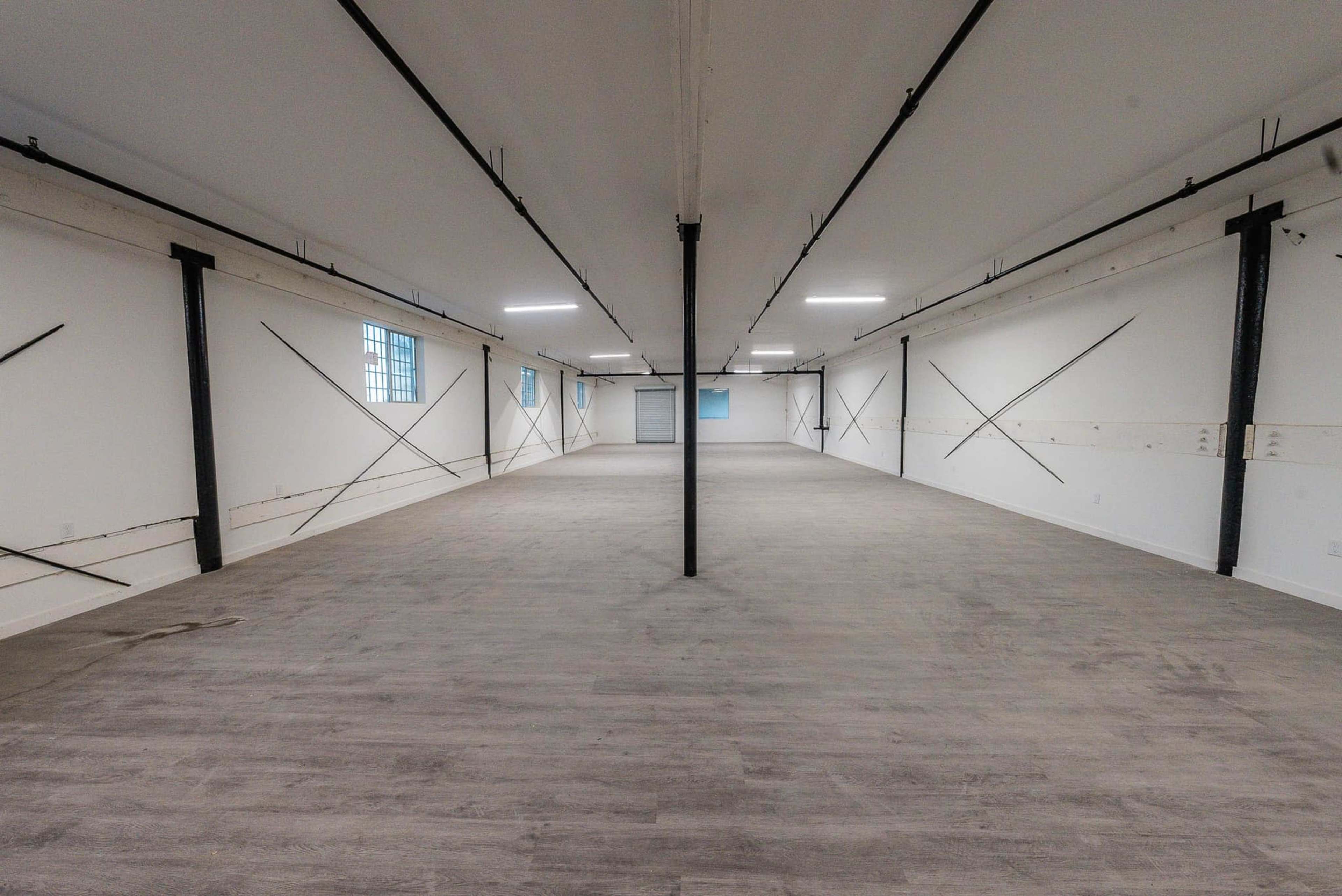 The image shows a large, empty room with a smooth floor, white walls, and exposed structural beams.