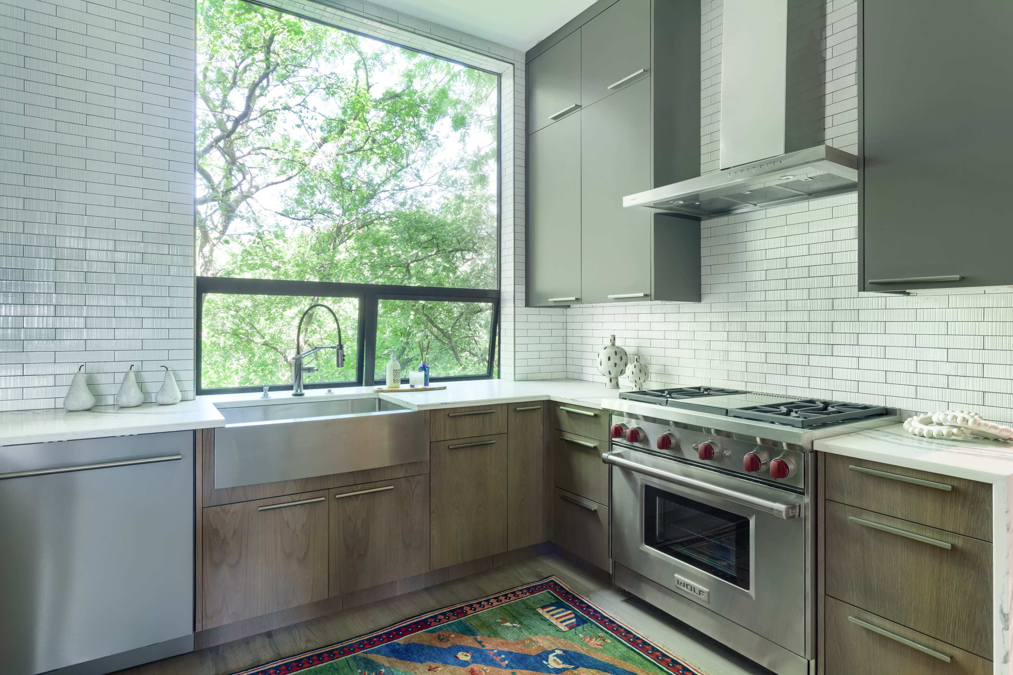 A modern kitchen features dark cabinetry, a large window with a view of greenery, and a gas range beneath a stainless steel hood.
