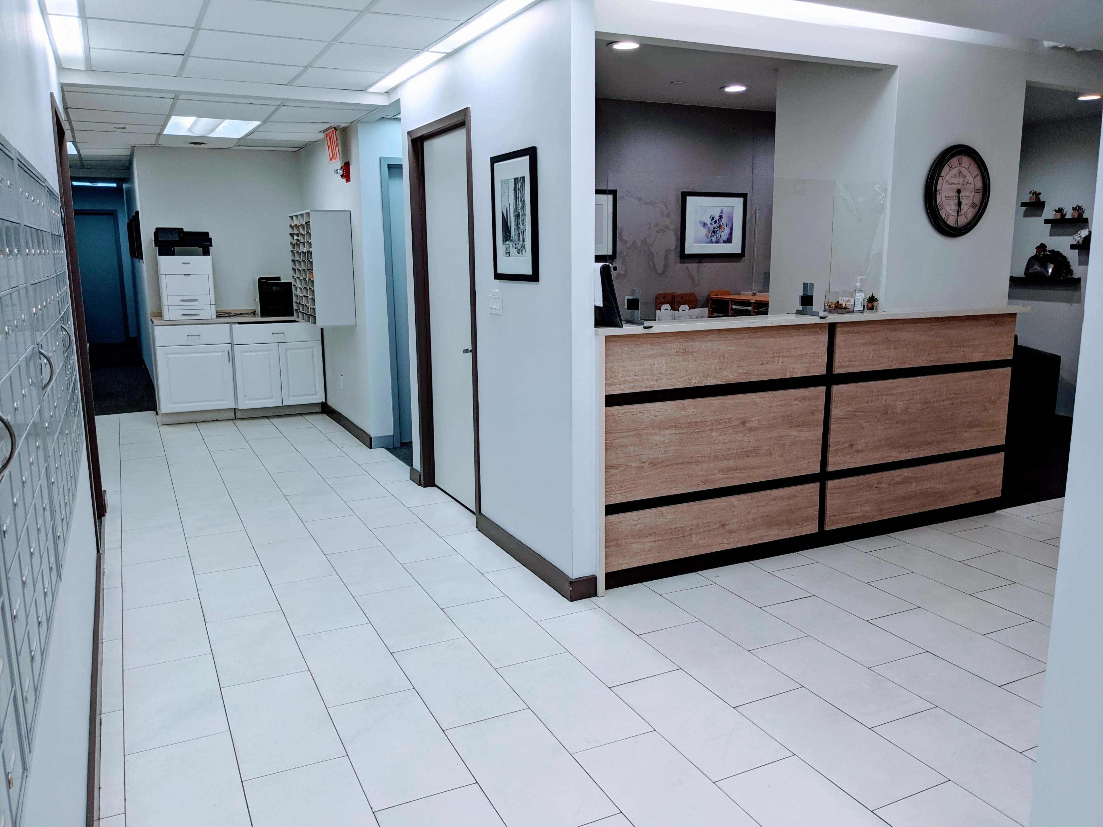 The image shows a well-lit hallway leading to a reception area with a wooden front desk and mailboxes on the left side.