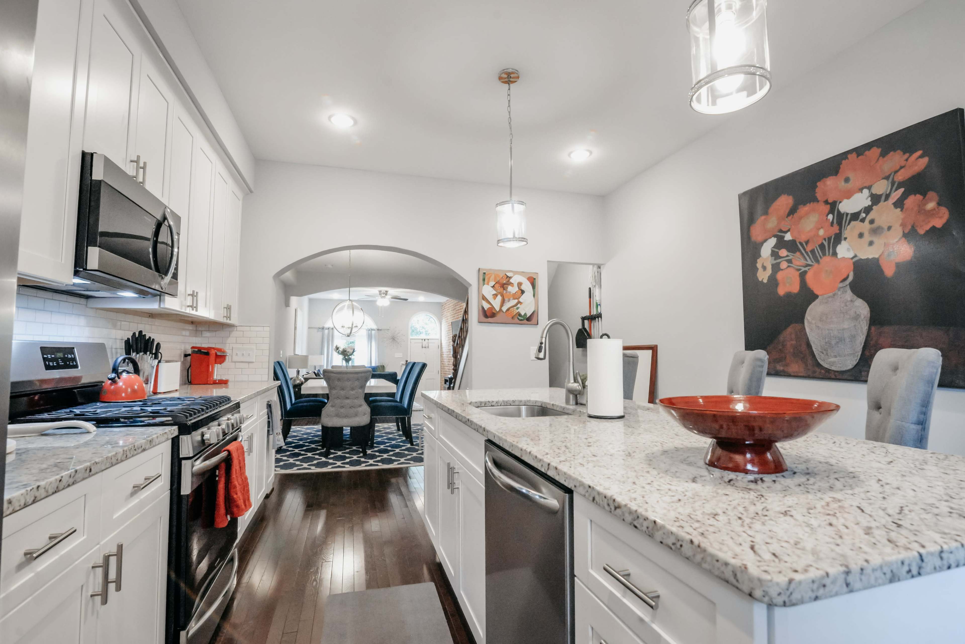 The image shows a modern kitchen with white cabinets, stainless steel appliances, and a granite countertop, leading into a dining area framed by an arched doorway.