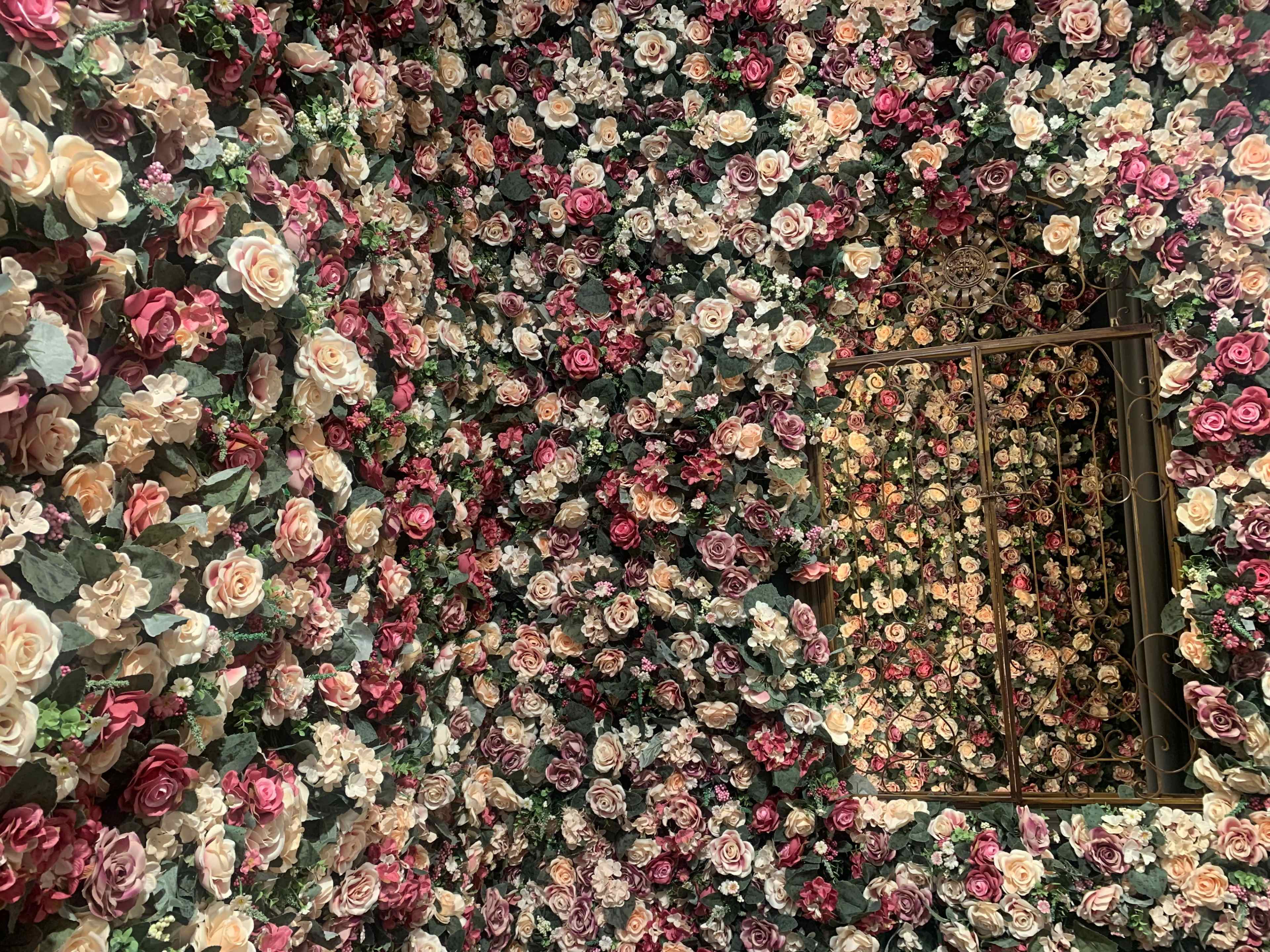 A room with walls covered in artificial roses in various colors, along with a decorative iron grill window.