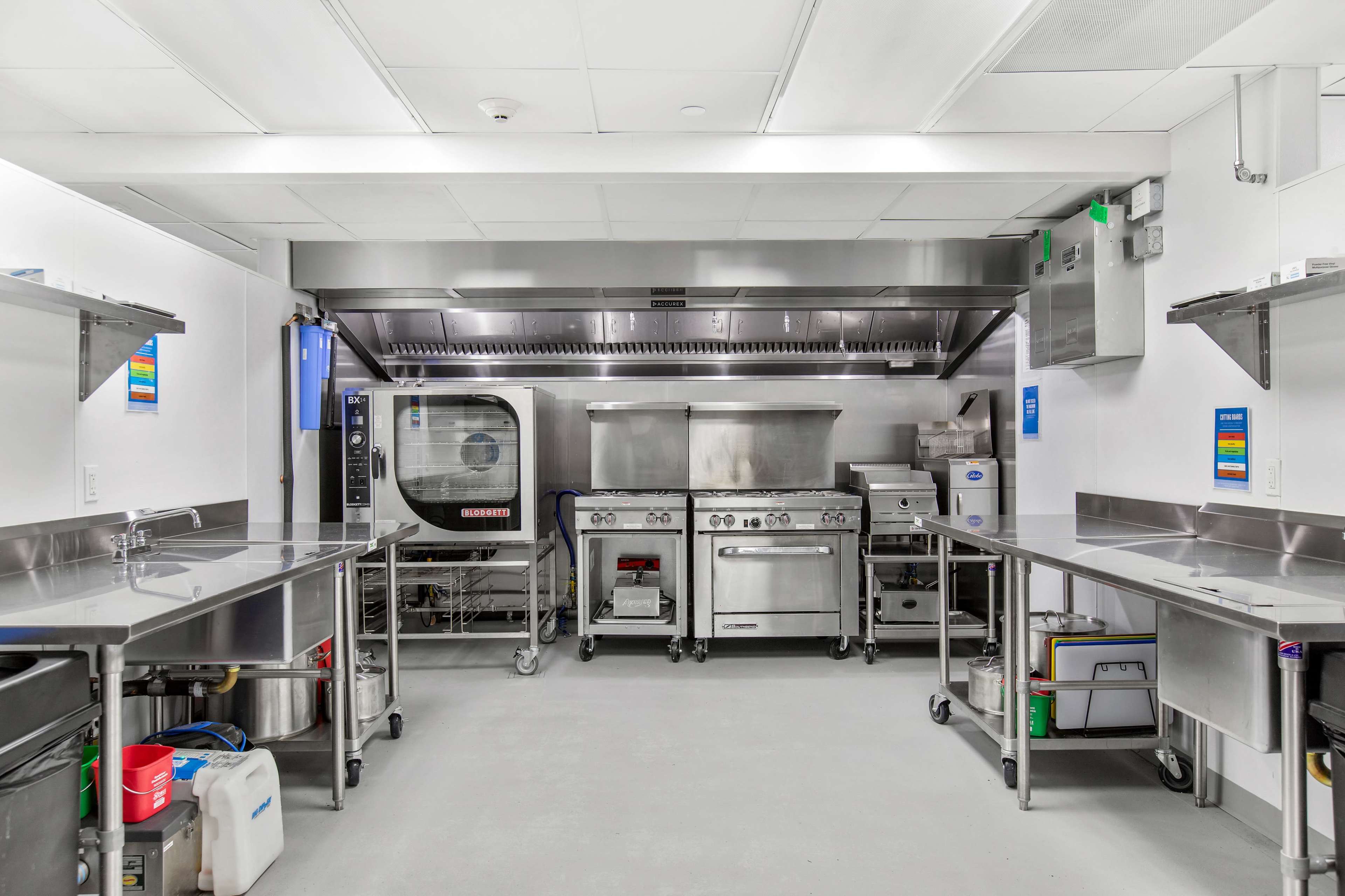 A commercial kitchen with stainless steel countertops, cooking equipment, and organized shelving.