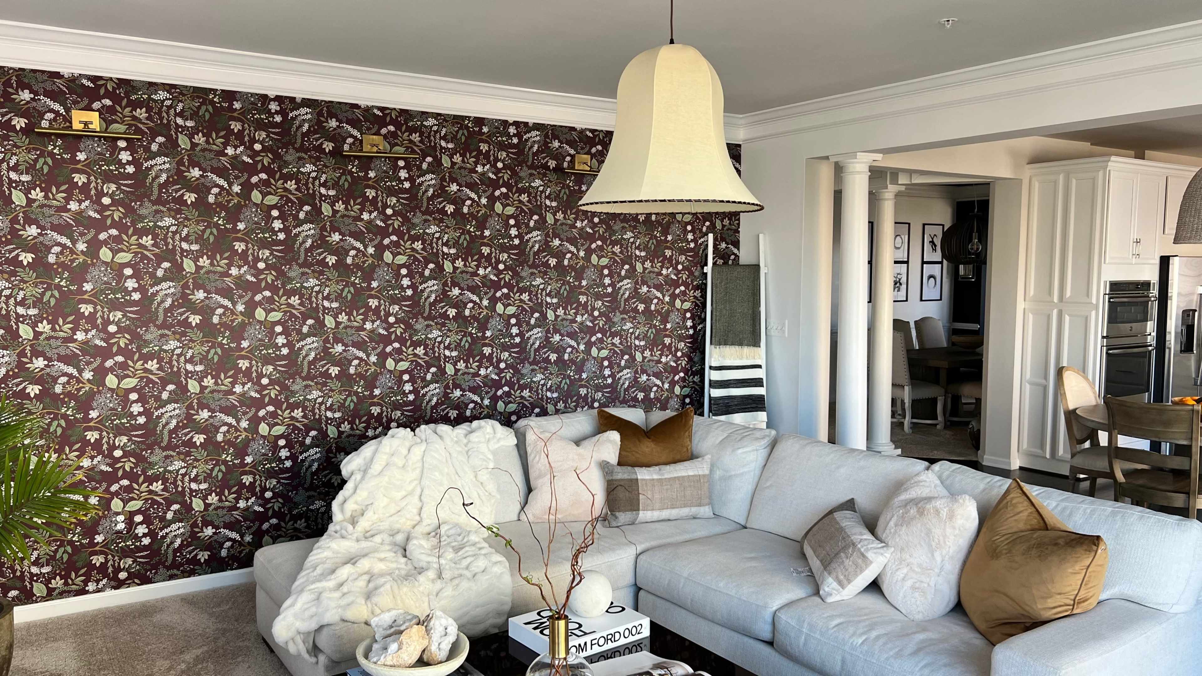 The living room features a floral-patterned wallpaper, a light-colored sectional sofa with decorative pillows, and a pendant light above.