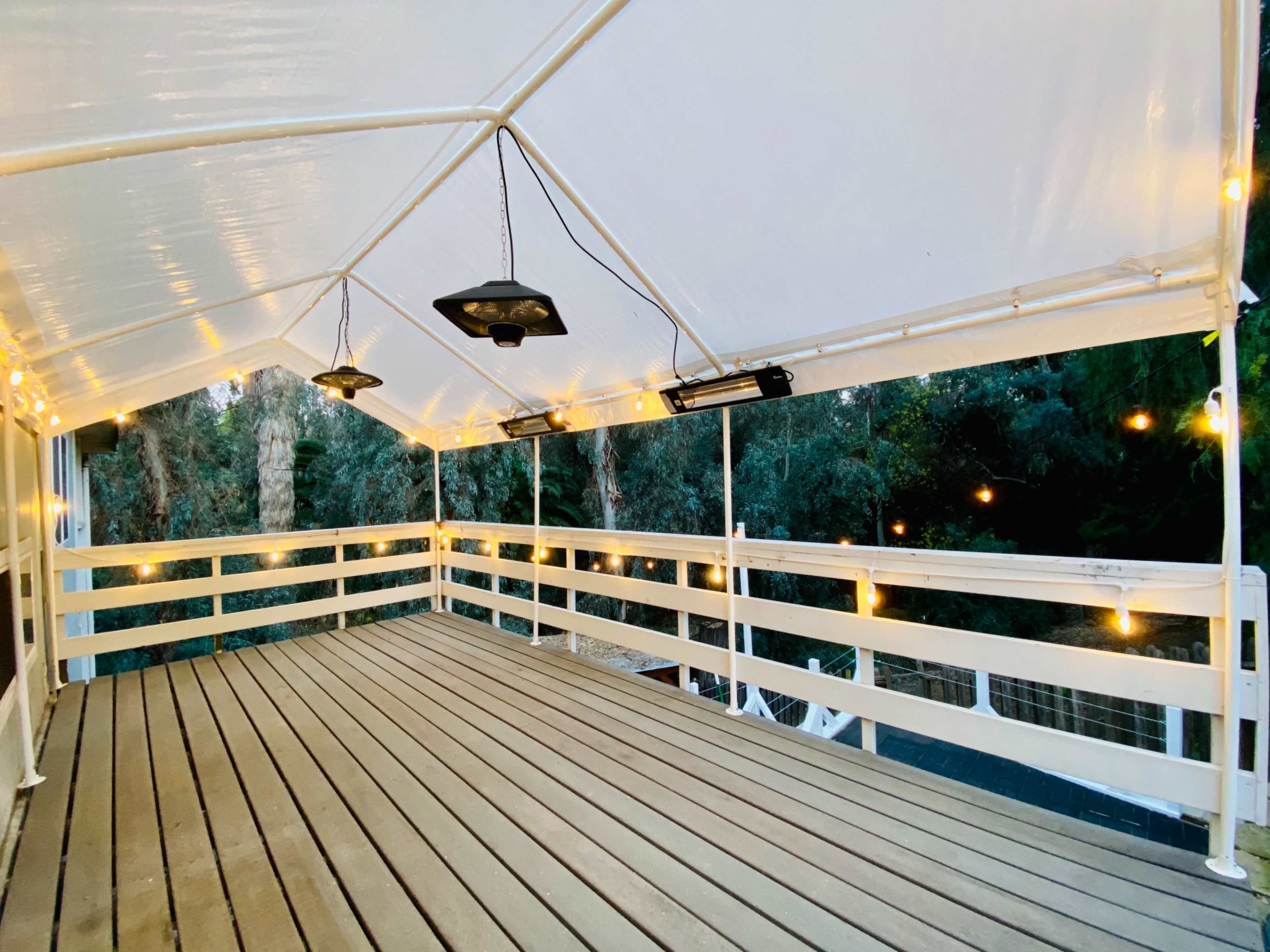The image shows a spacious, covered deck with wooden flooring and string lights hanging along the perimeter.