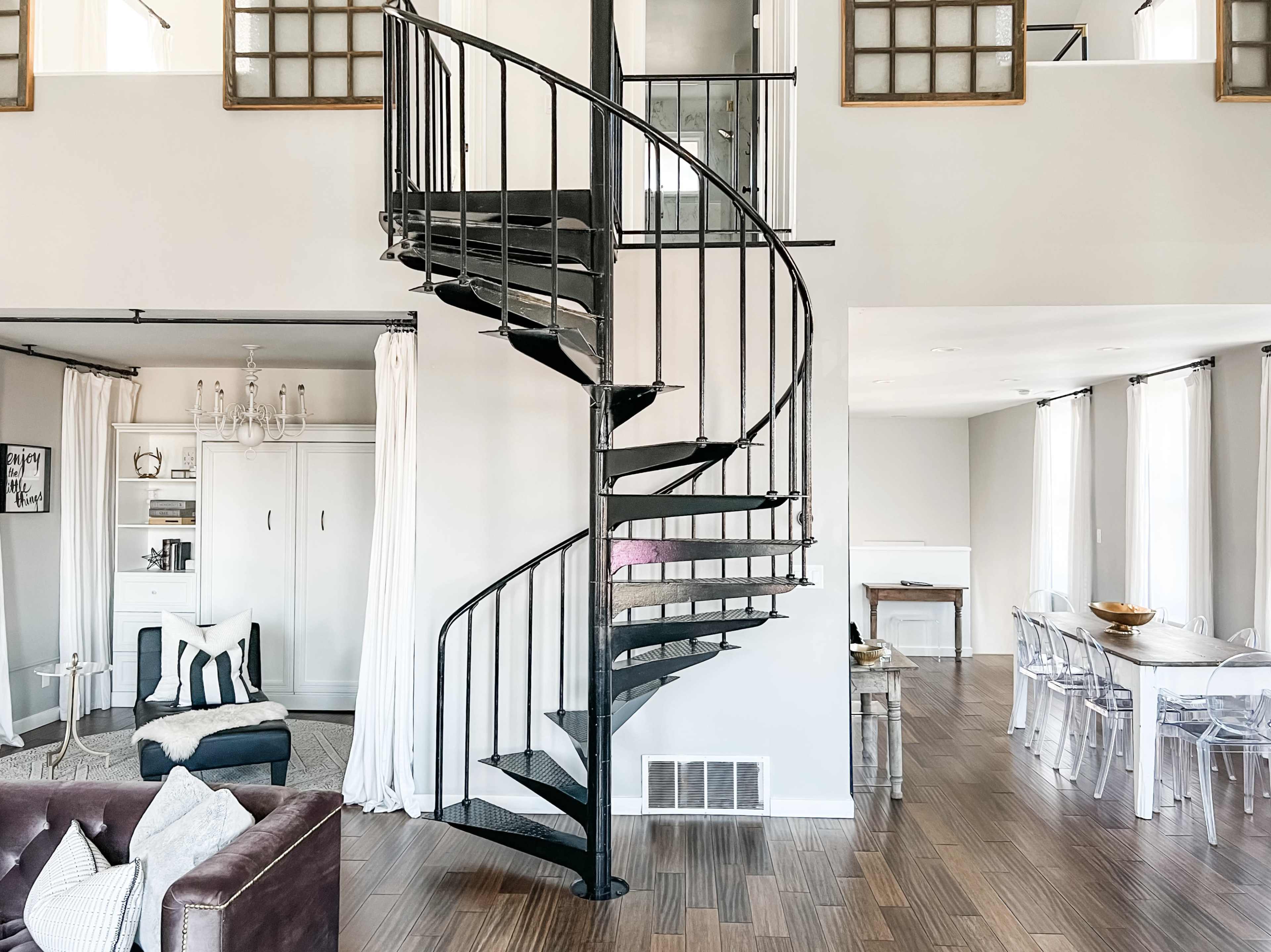 The image features a modern living space with a spiral staircase, wooden flooring, and large windows, creating an open and airy atmosphere.