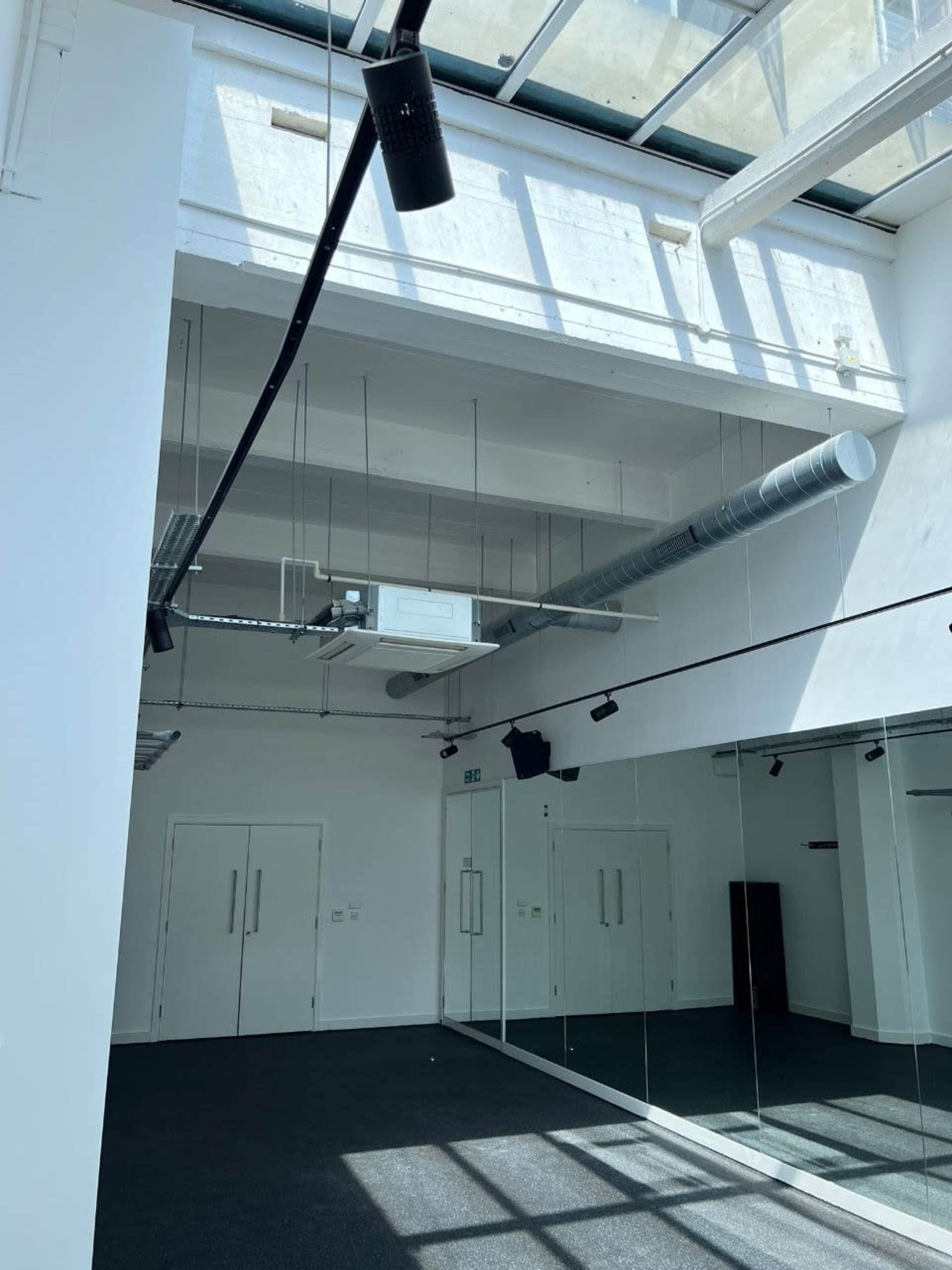 The image shows an empty, modern room with large windows, high ceilings, and mirrored walls.