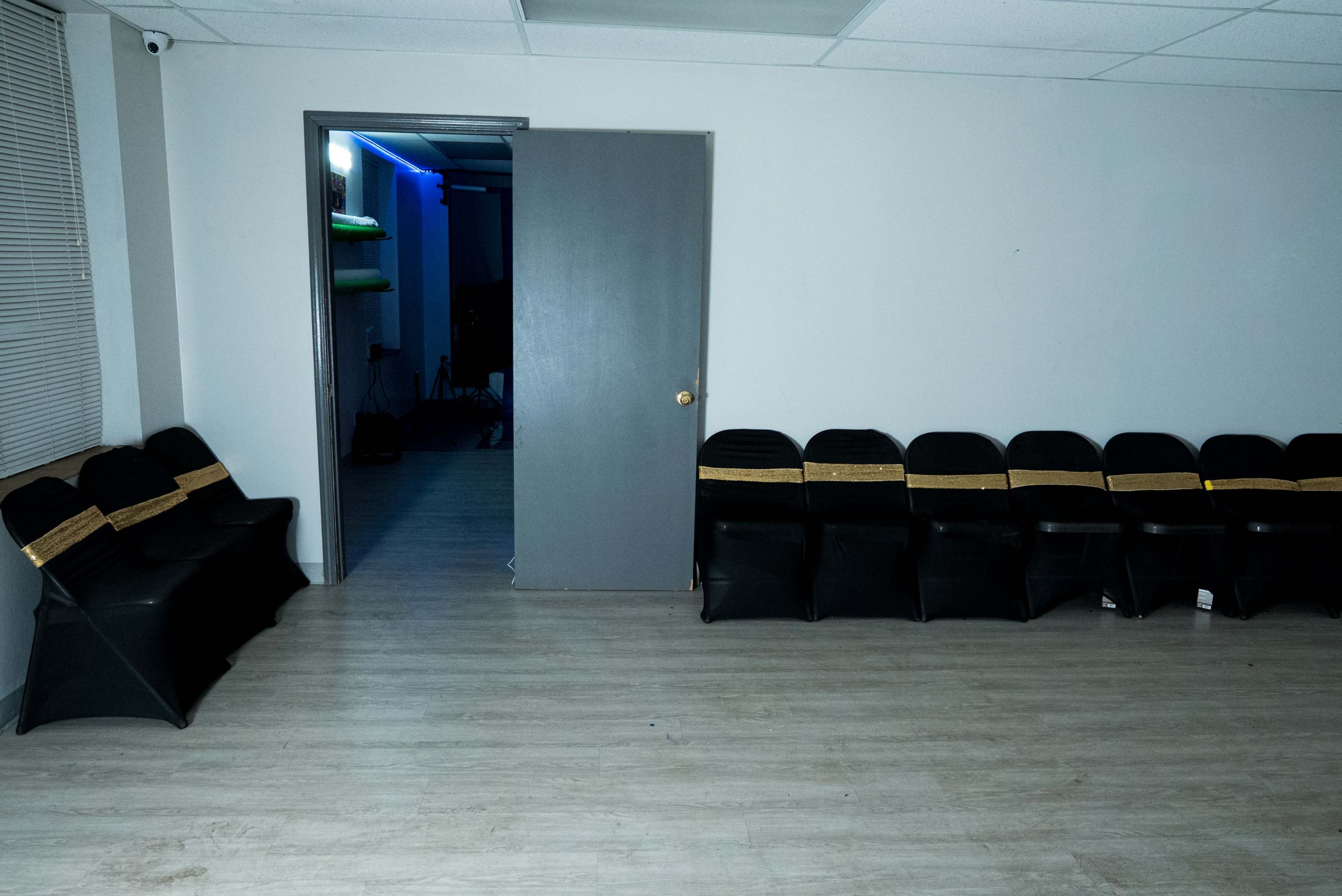 The image shows a room with a row of black chairs along one wall and a door leading to another space.