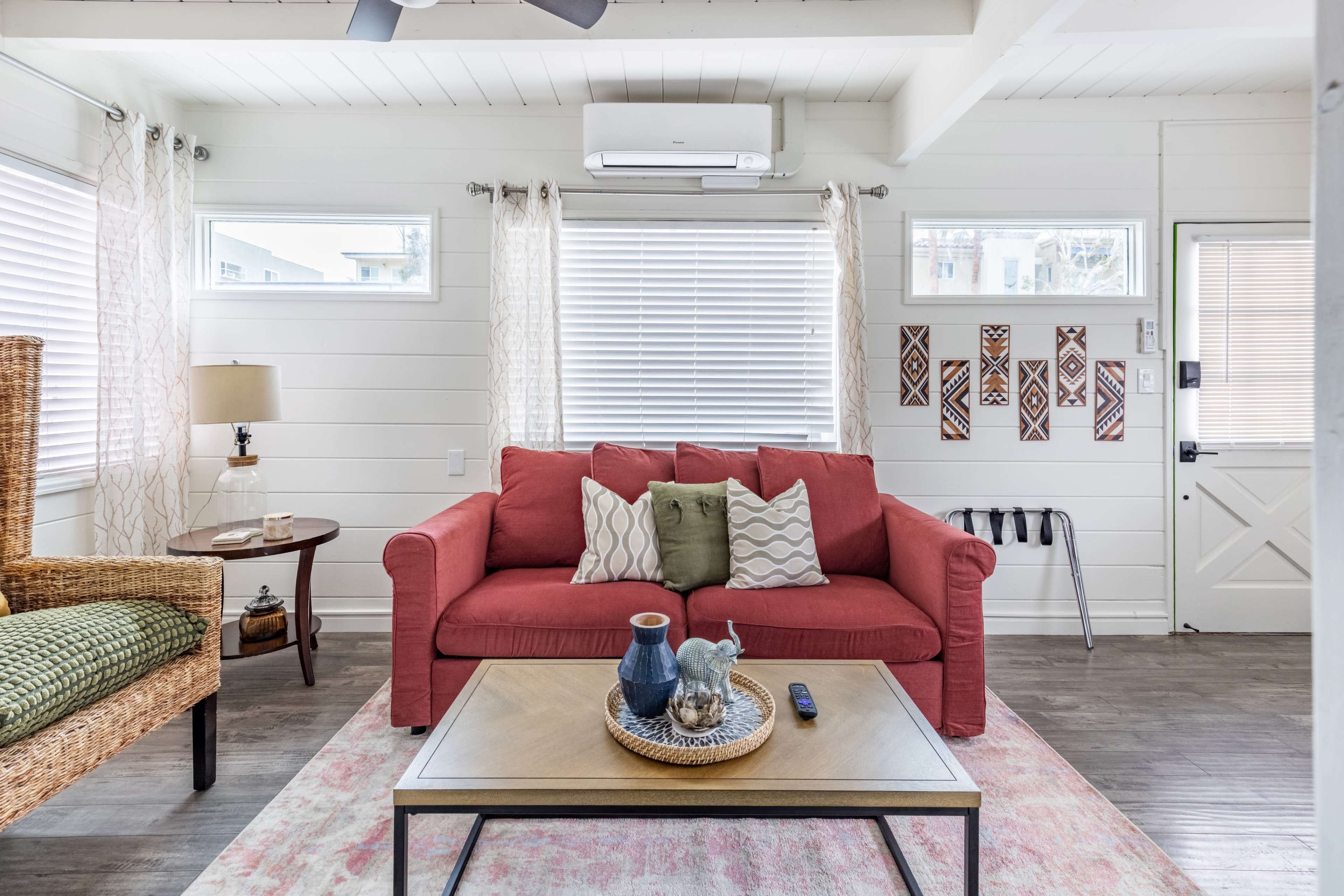A cozy living room featuring a red sofa, a coffee table with decorative items, and window treatments allowing natural light.