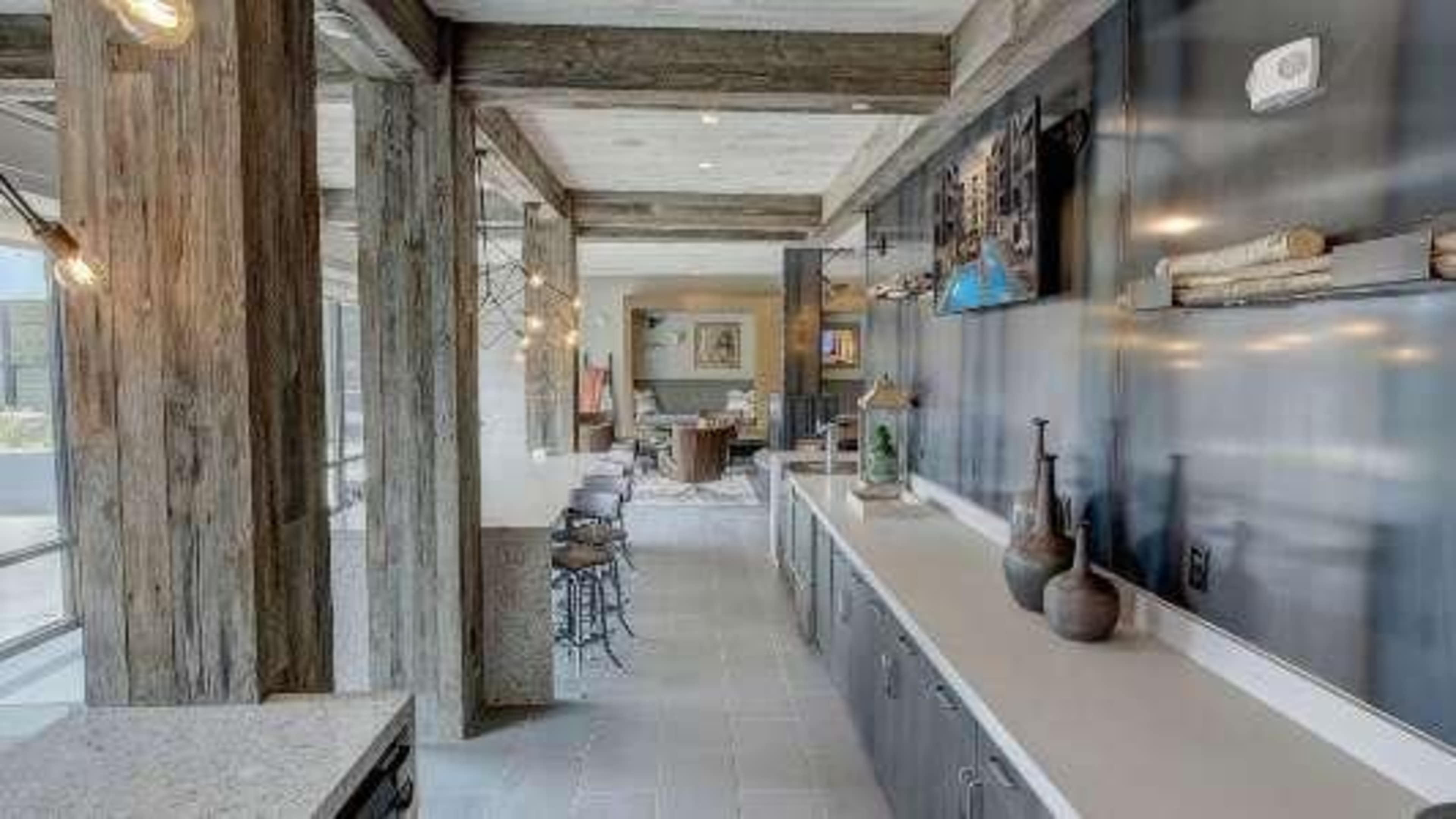 A modern interior space featuring wooden beams, a sleek countertop, and decorative vases, with a view of a dining area in the background.
